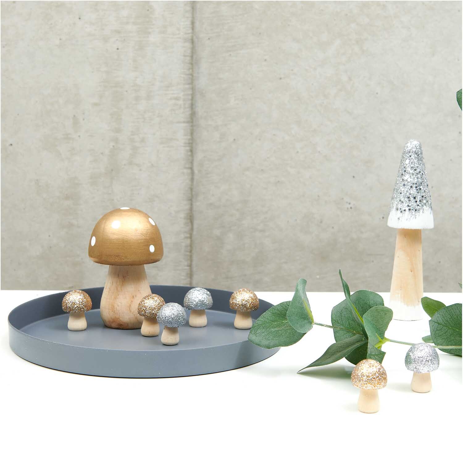 3D-Holzstreu Pilz mit Glitter silber 30x23mm 6 Stück von Rico Design 3D-Holzstreu Pilz mit Glitter in Silber auf grauem Tablett, dekoriert mit weiteren Pilzen und einem Baum. Ideal für festliche Dekorationen.