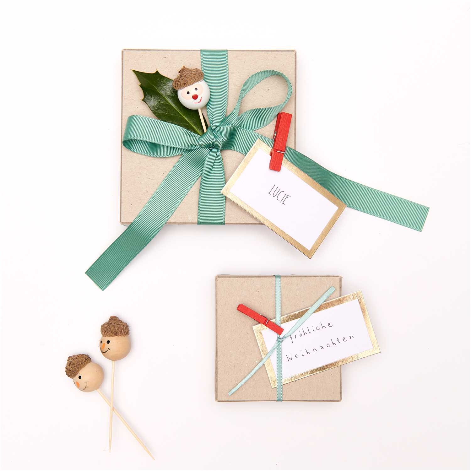 Sticks Schneemann natur 3 Stück von Rico Design Sticks Schneemann natur 3 Stück: Zwei dekorative Geschenkboxen mit Schneemann-Sticks und grünen Schleifen, ideal für festliche Anlässe.