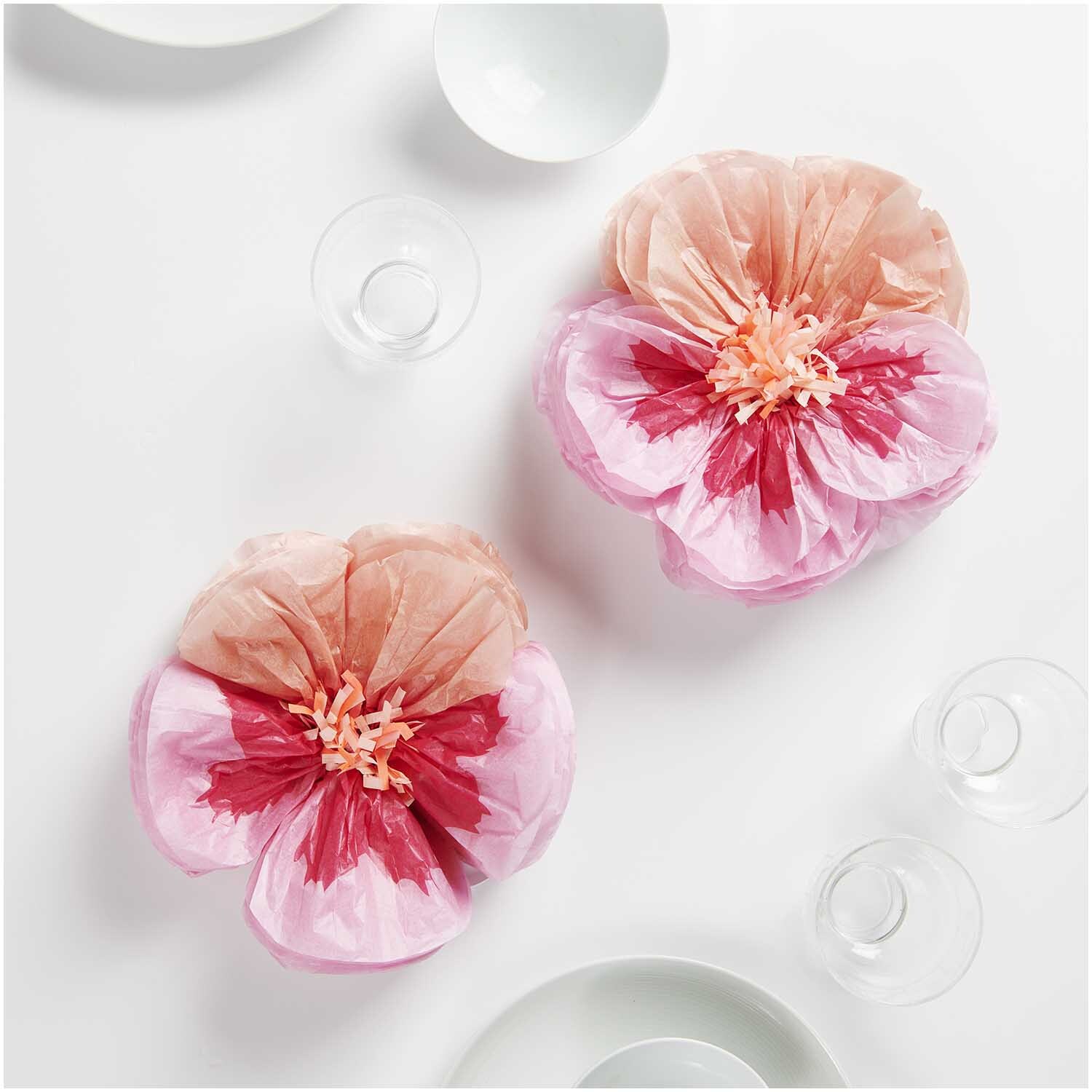 Seidenpapierblumen Stiefmütterchen von Rico Design in Pink, dekorativ arrangiert auf einem Tisch mit Geschirr.