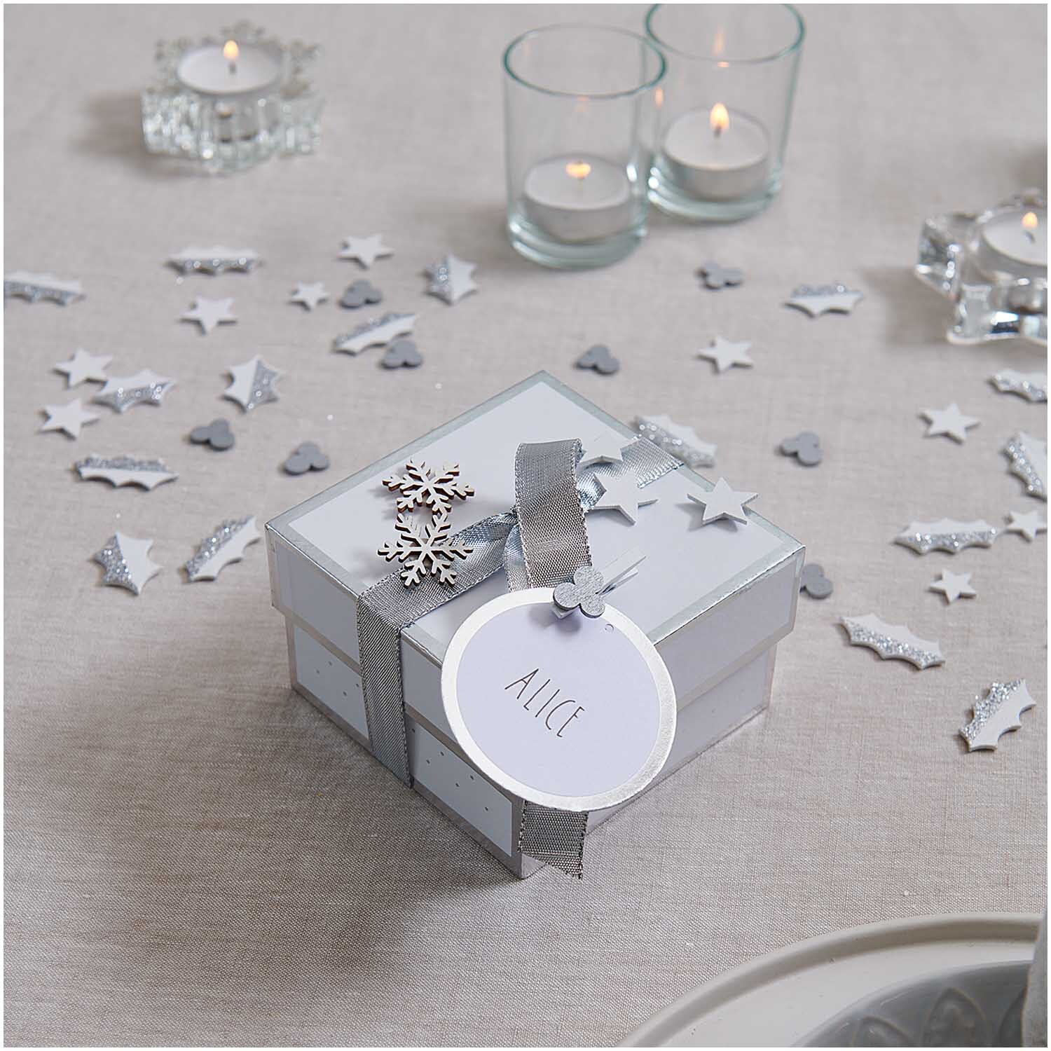 Dekoklammern Ilex weiß 8 Stück von Rico Design Dekoklammern Ilex weiß 8 Stück: Elegante Geschenkbox mit silbernem Band, umgeben von Kerzen und Streudeko.