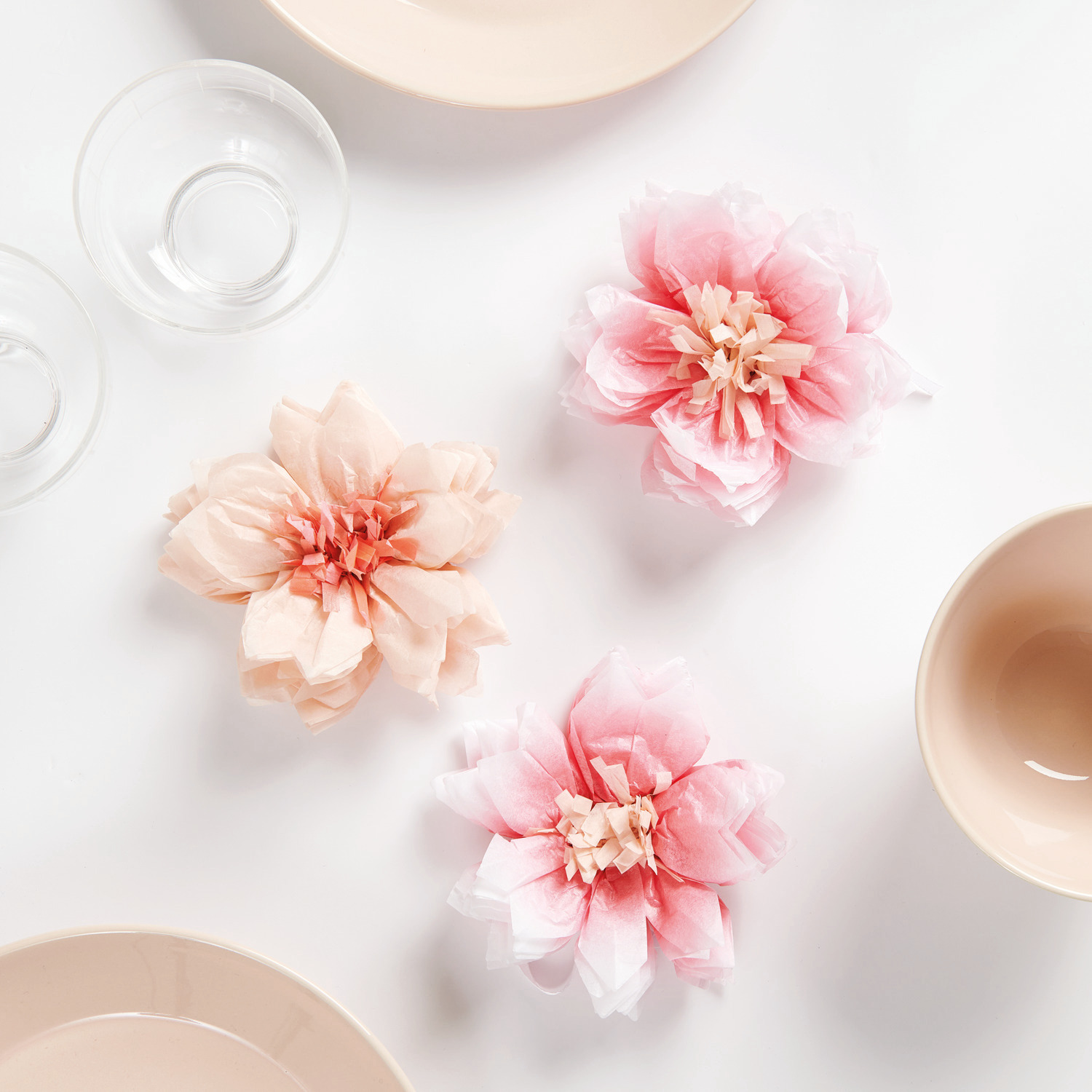 Seidenpapierblumen Kirschblüten, zartrosa und creme, dekorativ arrangiert auf weißem Hintergrund.
