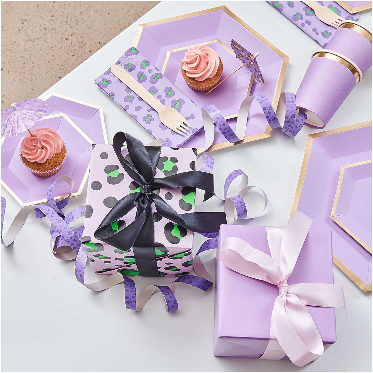 Paper Poetry Geschenkpapier Acid Leo rosa 70cm 3m 70g/m² von Rico Design Paper Poetry Geschenkpapier Acid Leo rosa umhüllt Geschenke, umgeben von lila Partygeschirr und Cupcakes.
