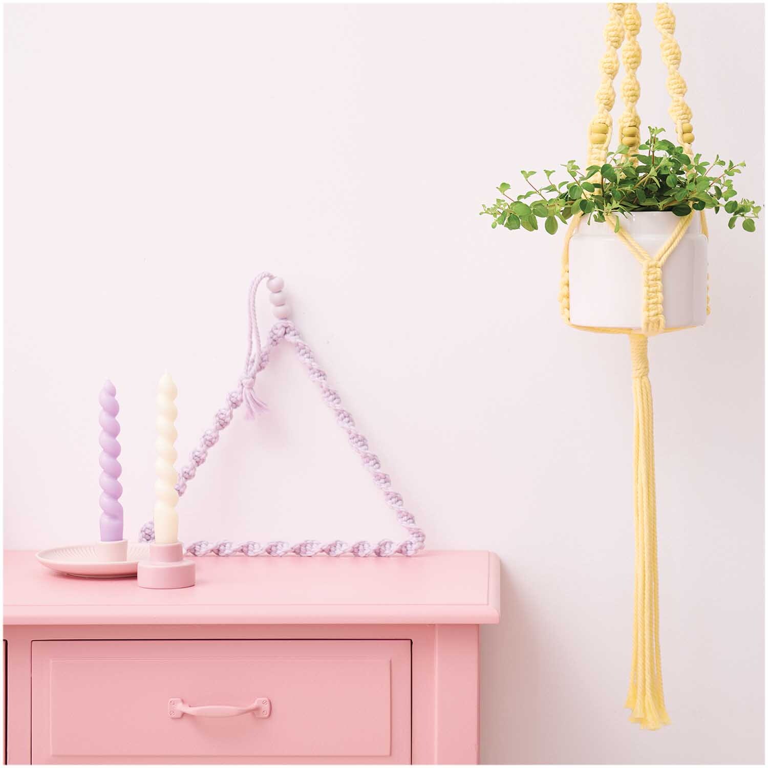Creative Cotton Cord Makramee-Garn in Pastellgelb, dekoriert als Pflanzenhänger neben pastellfarbenen Kerzen auf rosa Kommode.