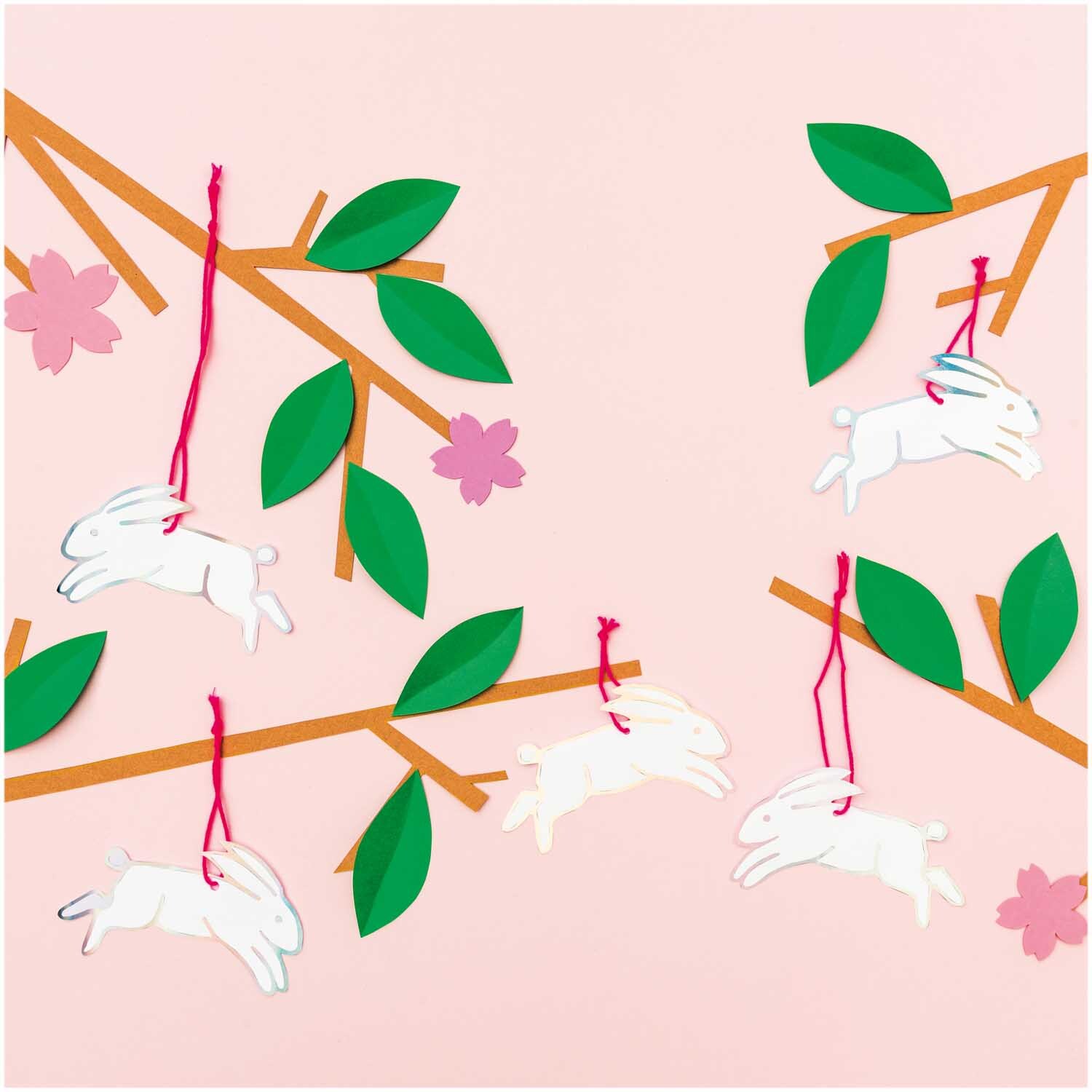 Paper Poetry Papieranhänger Hasen: Weiße Hasenanhänger von Rico Design an Ästen mit grünen Blättern und rosa Blüten.