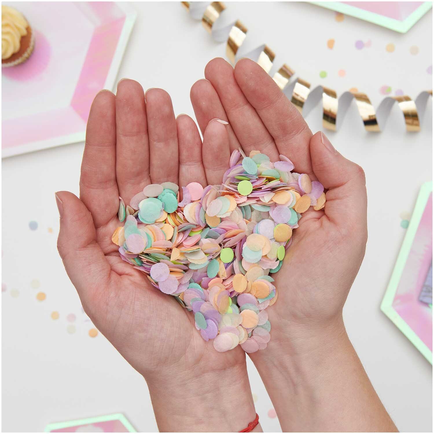 Konfetti Pastell Rainbow Mix 20g von Rico Design Konfetti Pastell Rainbow Mix 20g in Händen gehalten, umgeben von Partydekorationen, ideal für Feiern.