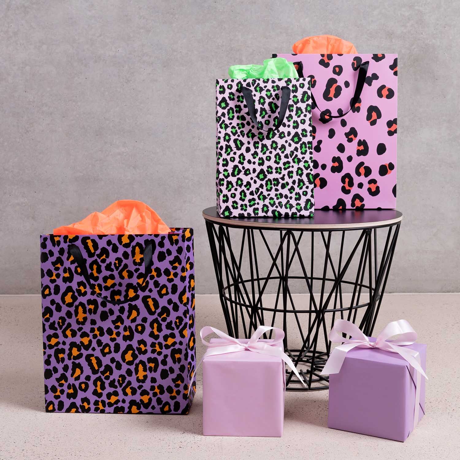 Paper Poetry Geschenktüte Acid Leo pink 26x32x12cm von Rico Design Paper Poetry Geschenktüte Acid Leo pink mit Leopardenmuster, umgeben von weiteren bunten Tüten und Geschenken.