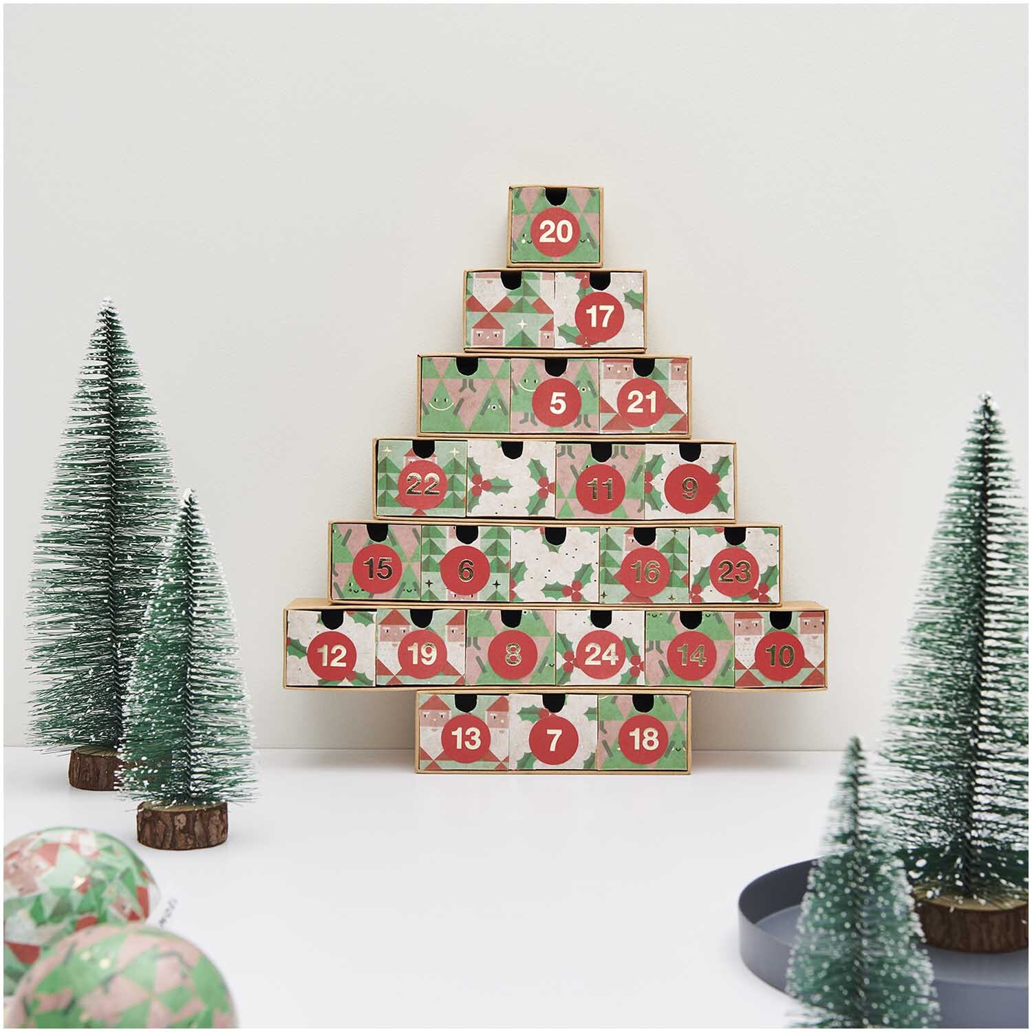 Paper Poetry Paper Patch Papier Weihnachtsmann 30x42cm: Adventskalender in Tannenbaumform mit roten und grünen Details, umgeben von Miniaturtannenbäumen.