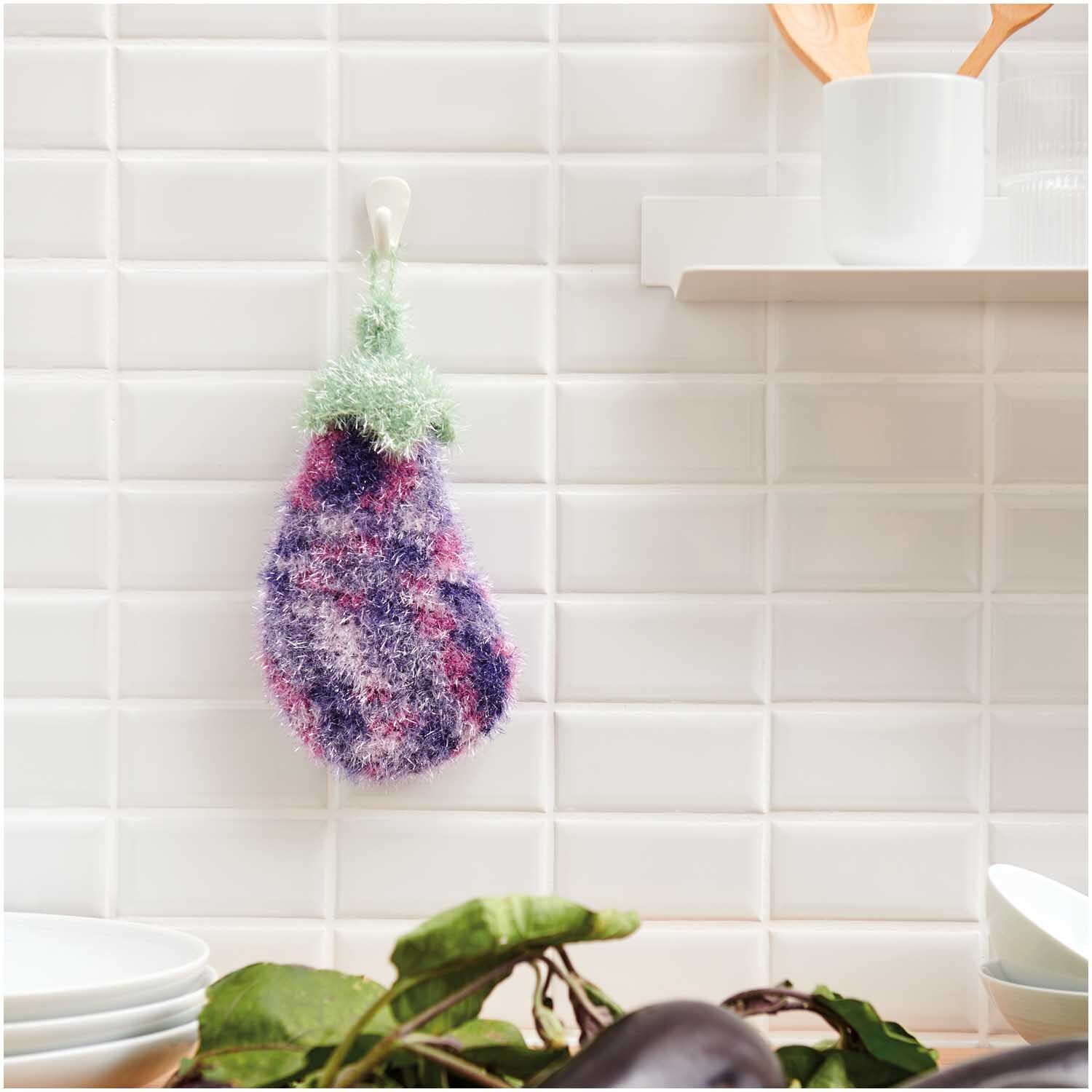 Creative Bubble Print: Ein gehäkelter Schwamm in Auberginenform hängt an einer weißen Kachelwand.