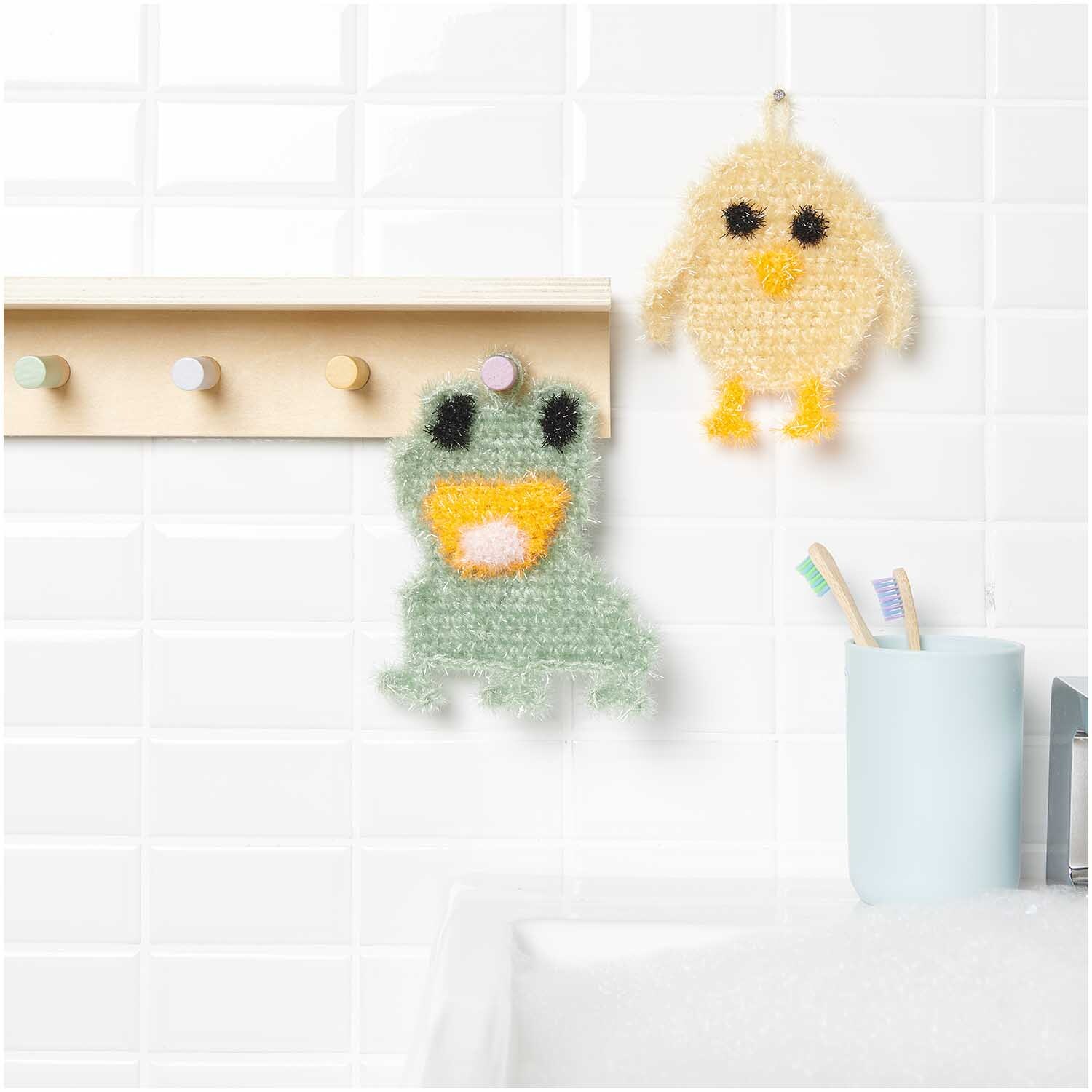 Häkelset Creative Bubble Kleine Tierchen von Rico Design Häkelset Creative Bubble Kleine Tierchen: Zwei gehäkelte Tierfiguren, Frosch und Küken, hängen in einem Badezimmer an Haken.
