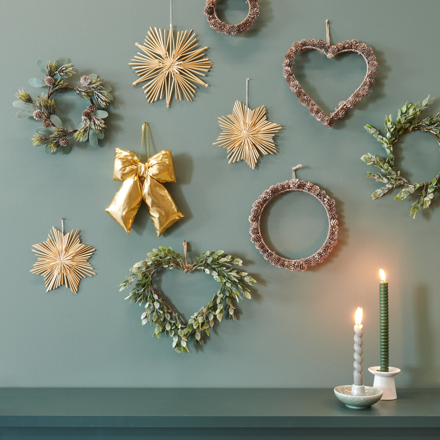 Lärchenzapfen-Herz Weiß: Wanddekoration mit goldener Weihnachtsschleife und grünen Blätterkränzen, ideal für festliche Anlässe.