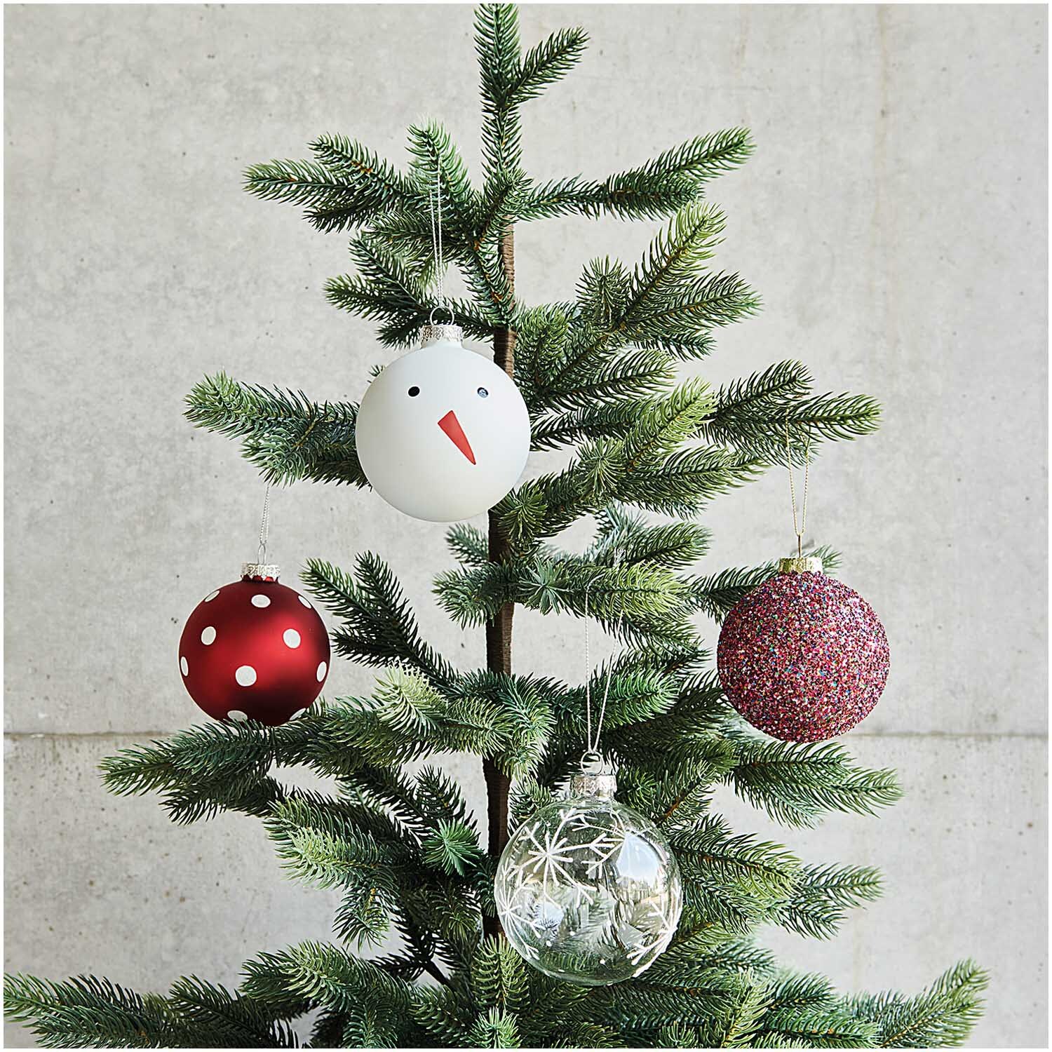 Glaskugel Baumschmuck Schneemann 8cm von Rico Design Glaskugel Baumschmuck Schneemann 8cm von Rico Design: Weißer Schneemann-Anhänger an einem Tannenbaum, umgeben von weiteren dekorativen Kugeln.