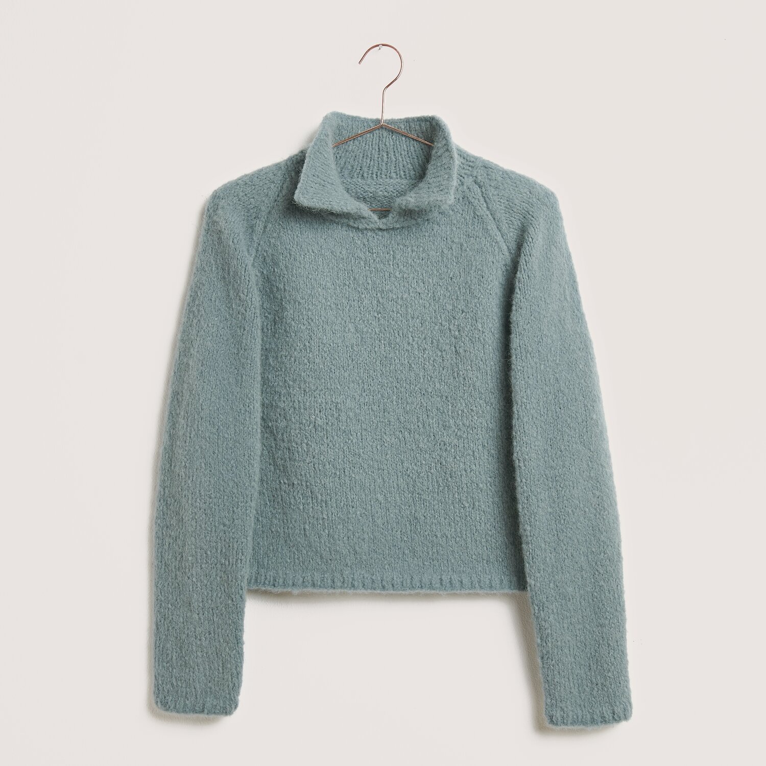 Luxury Pure Baby Alpaca 50g 150m Farbe Rauchblau von Rico Design Strickset Pullover Modell 13a aus Made by Me No. 21 in Rauchblau, gefertigt aus Luxury Pure Baby Alpaca, präsentiert auf einem Kleiderbügel.