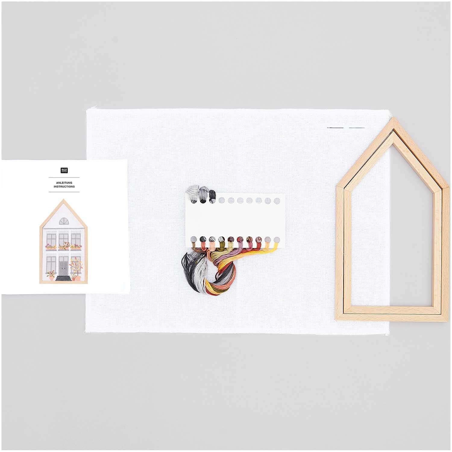 Paquet à broder Maison d'automne moyen 12x22,5cm 12x22,5cm from Rico Design Stickpackung Herbsthaus mittel 12x22,5cm von Rico Design zeigt ein Set mit Garn, Stoff und Holzrahmen in Hausform für kreative Stickprojekte.
