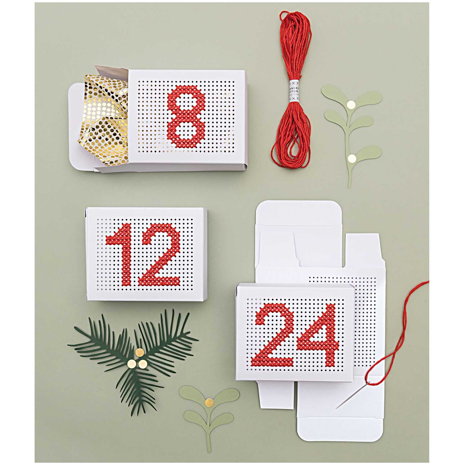 Paper Poetry Adventskalender Boxen zum Besticken Farbe Weiß von Rico Design Paper Poetry Adventskalender Boxen zum Besticken von Rico Design, dekoriert mit roten Zahlen und Garn auf grünem Hintergrund.