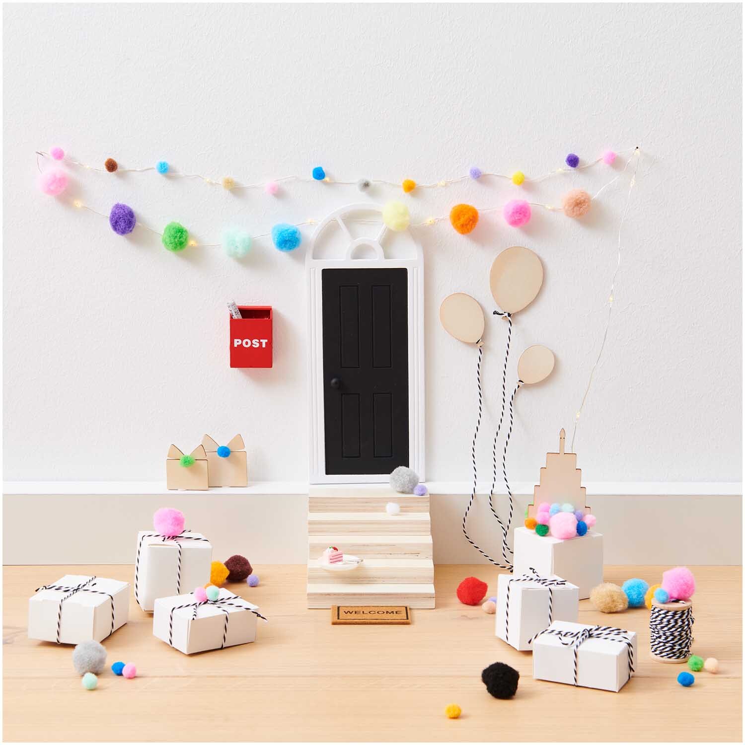 Miniatur Wichteltür mit Bogen, umgeben von bunten Pompons und Geschenken, von Rico Design.