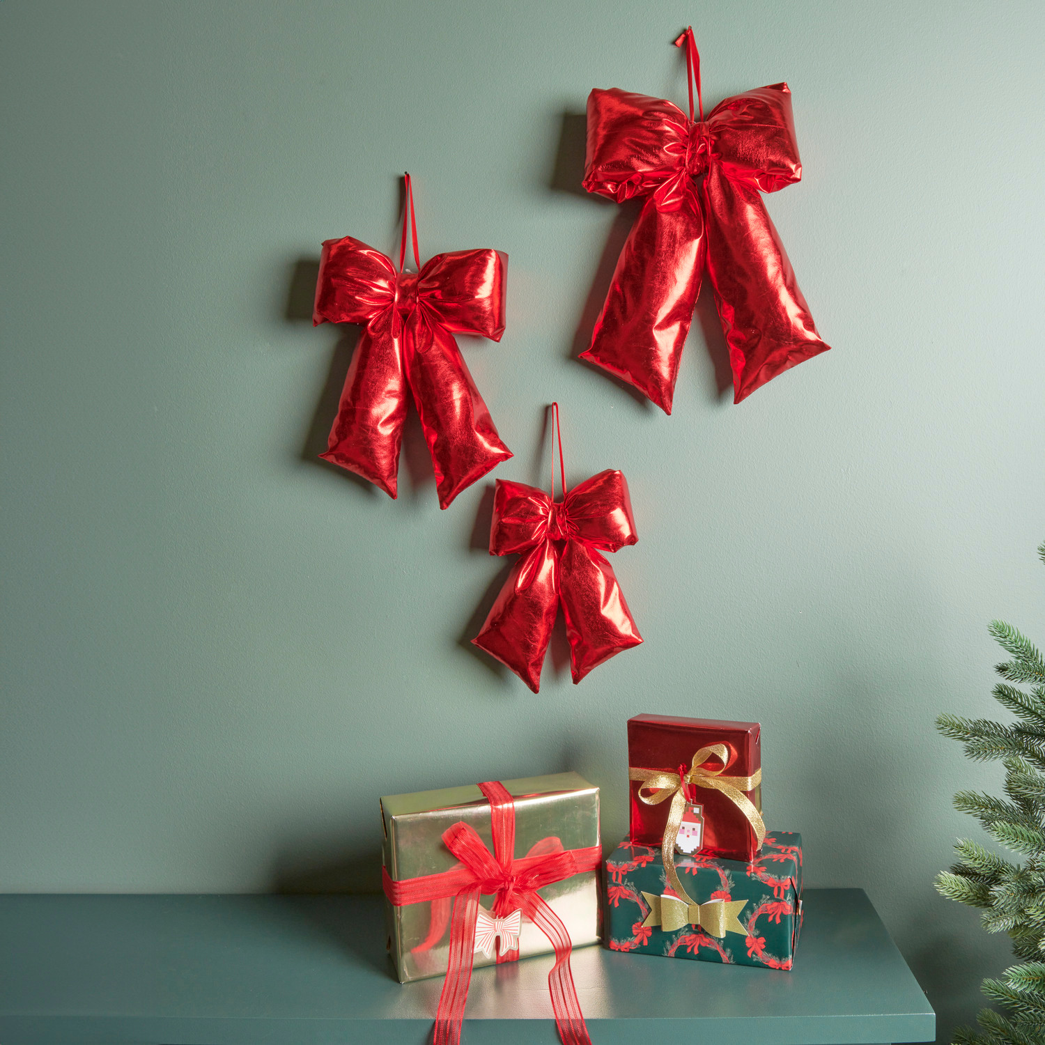 Paper Poetry 3D Sticker Schleifen Rot 4 Stück von Rico Design Weihnachtsschleife Rot: Drei glänzende 3D-Sticker-Schleifen von Paper Poetry an grüner Wand.