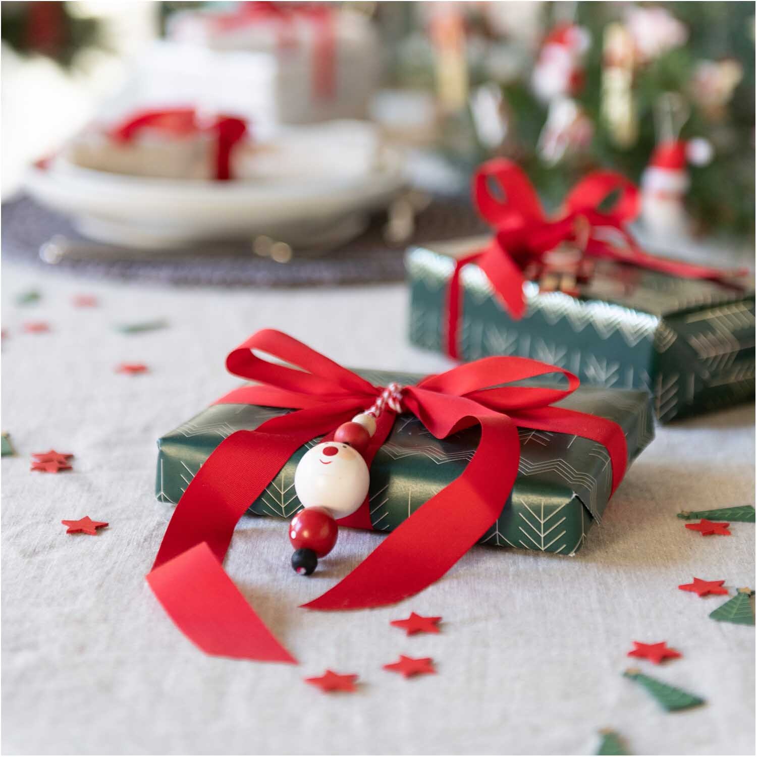 Holzstreu Ilex grün-rot 48 Stück dekoriert einen festlichen Tisch mit Geschenken und roten Schleifen.