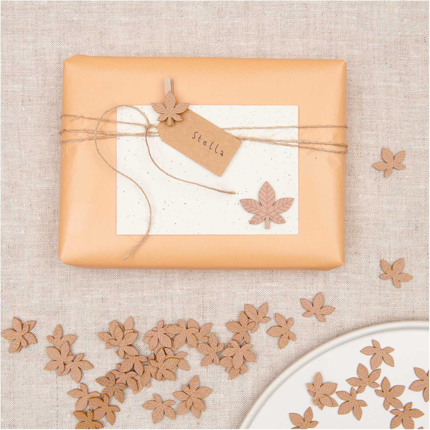 Holzsticker Blatt braun 12 Stück von Rico Design Holzsticker Blatt braun 12 Stück dekorieren ein Geschenk mit Etikett auf beigem Stoff. Ideal für kreative Bastelprojekte.