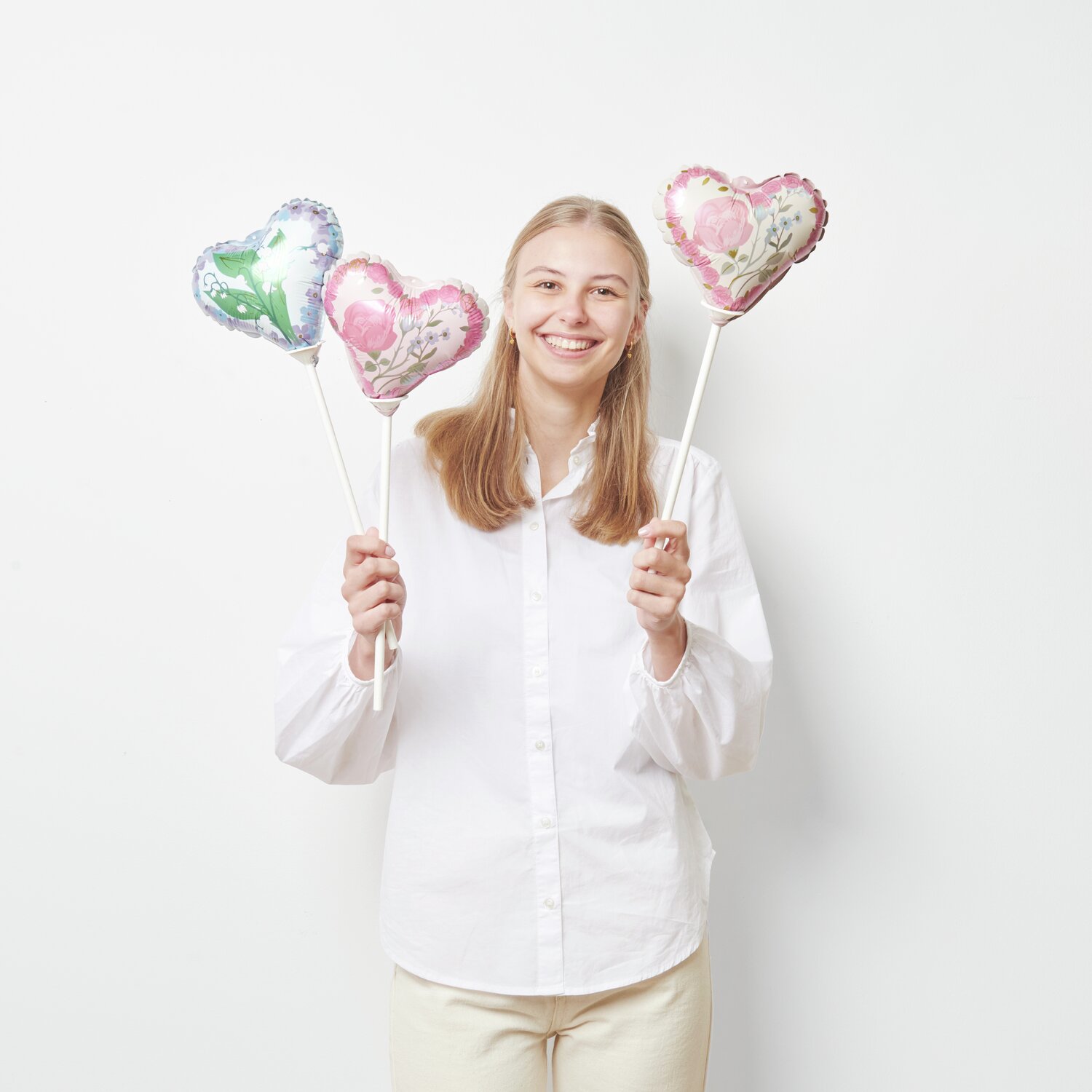 Mini-Folienballon Set Herzen mit Blumen von Rico Design, gehalten von einer lächelnden Person.