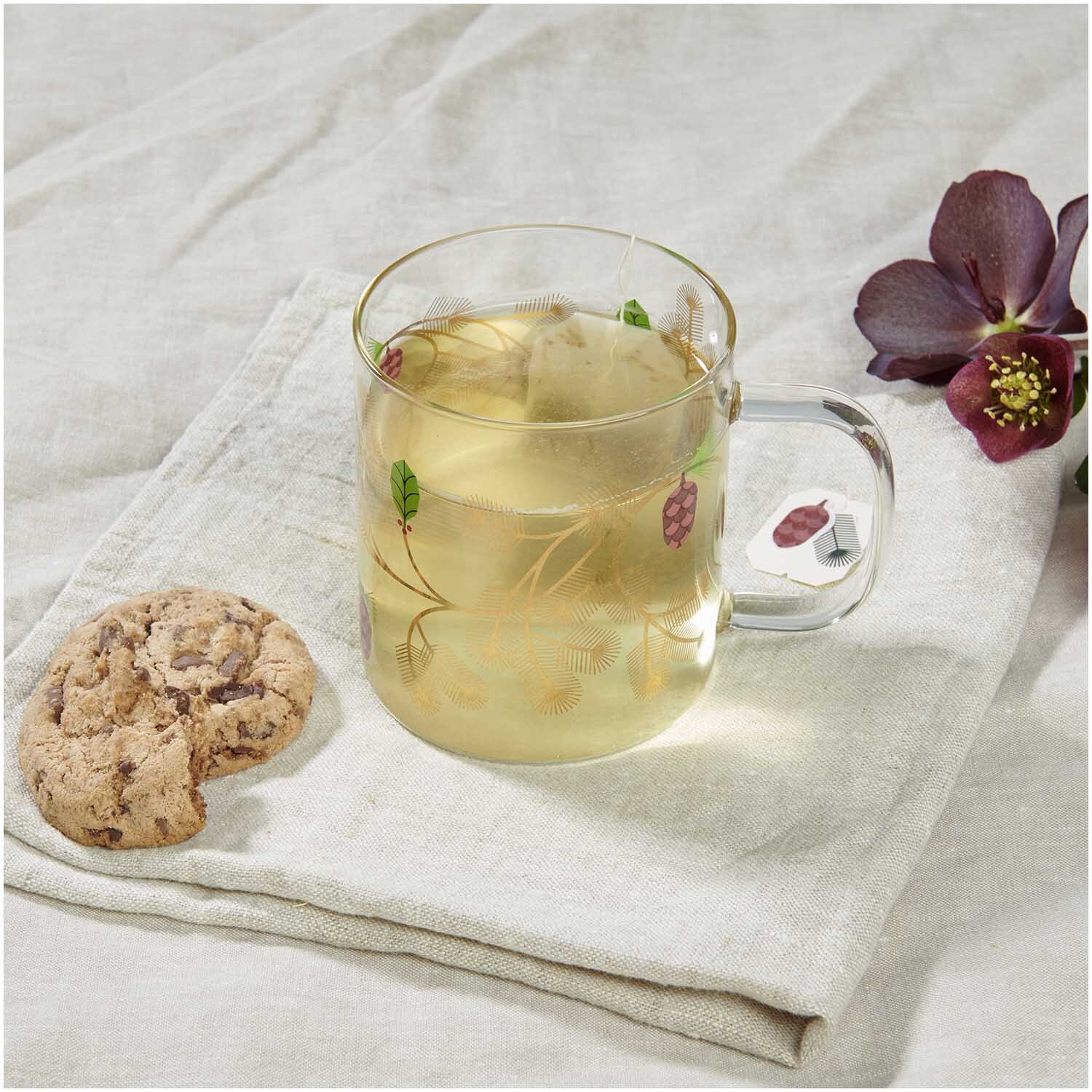 Glastasse Tannenzweig Ø8,5cm von Rico Design Glastasse Tannenzweig Ø8,5cm von Rico Design mit Tee gefüllt, auf Leinentuch neben Keks und Blume.