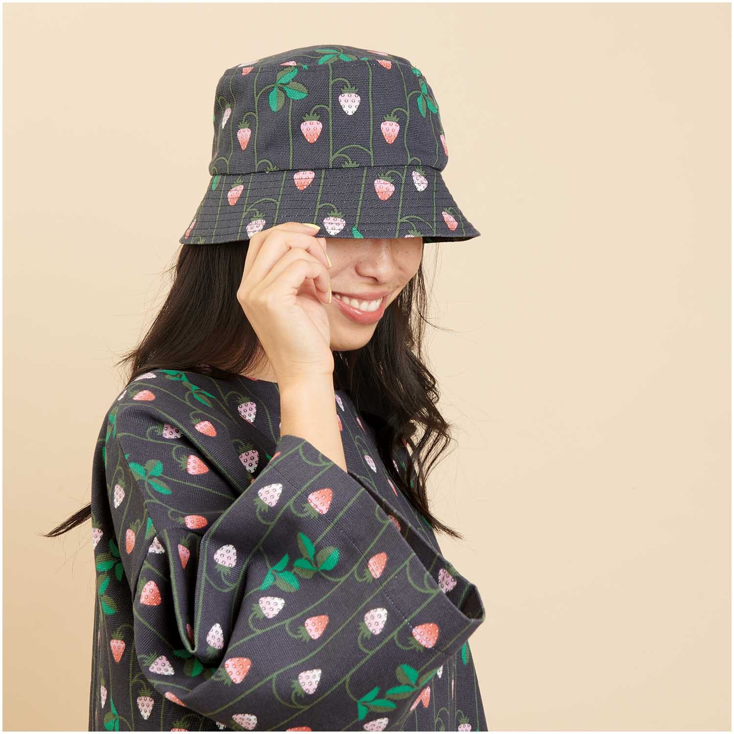 Meterware Canvas Erdbeeren blau von Rico Design Meterware Canvas Erdbeeren blau: Frau trägt Hut und Mantel mit Erdbeermuster von Rico Design.