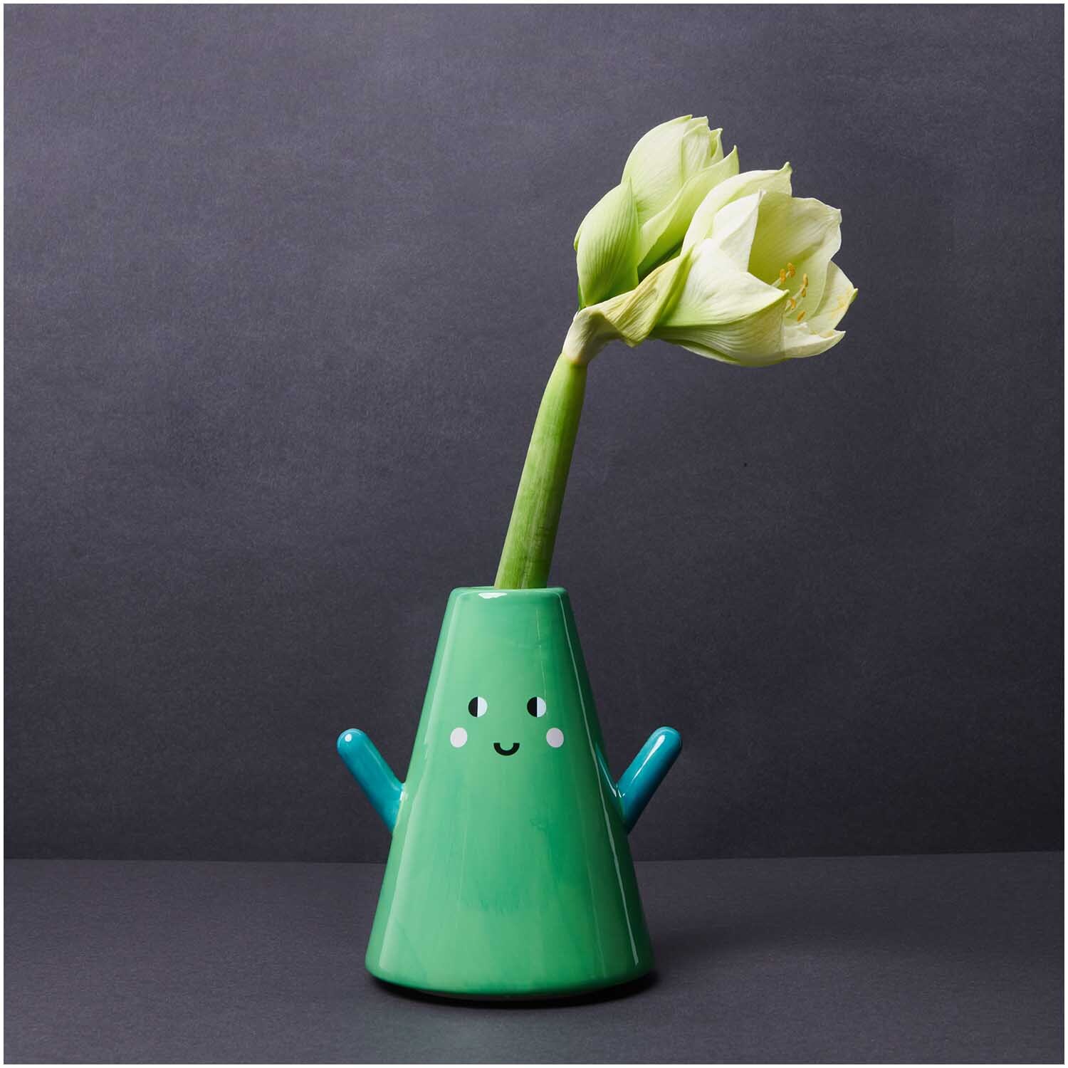 Keramik Vase Tanne grün 20cm von Rico Design Keramik Vase Tanne grün 20cm: Fröhliche, grüne Vase mit Gesicht und Blumen auf dunklem Hintergrund.