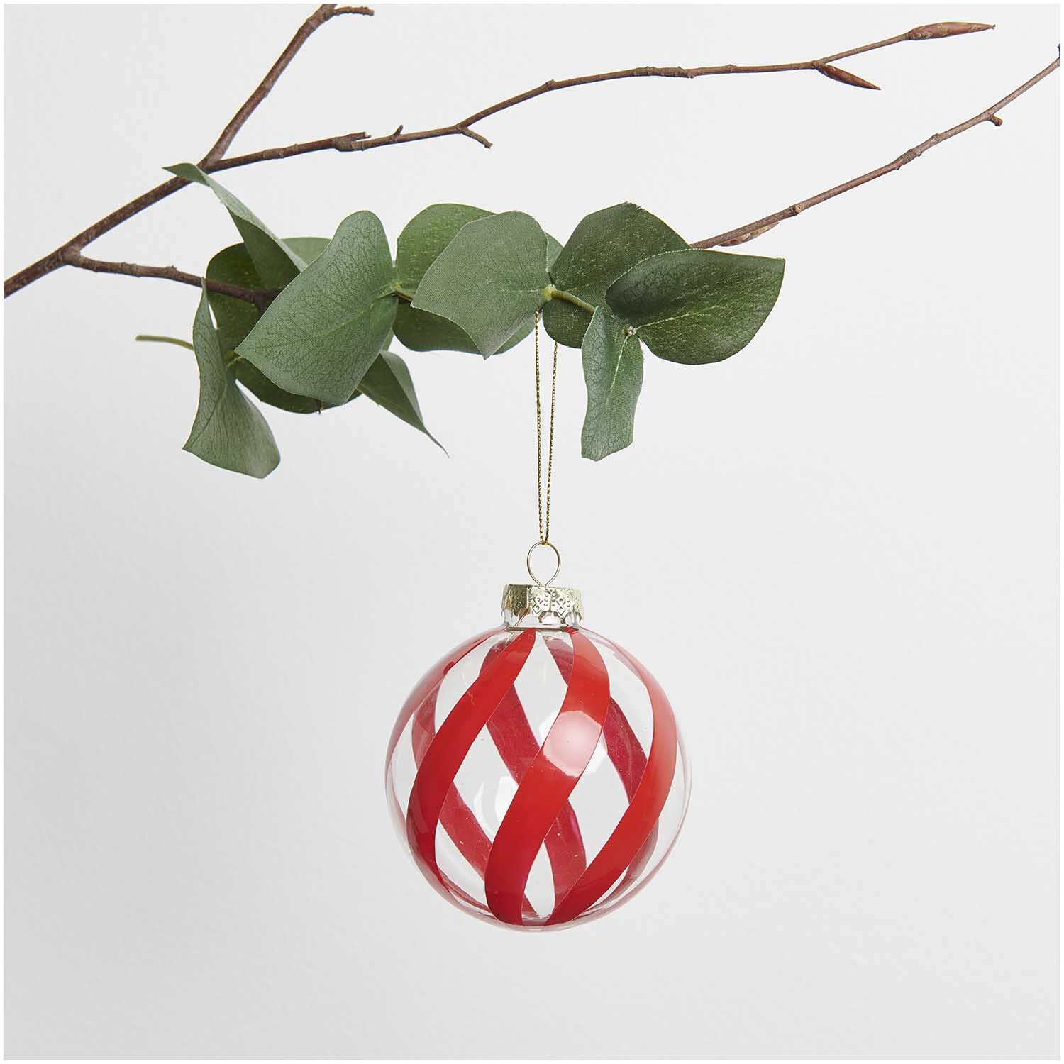 Glaskugel Baumschmuck mit rot-weißen Streifen, hängend an einem Ast mit grünen Blättern.