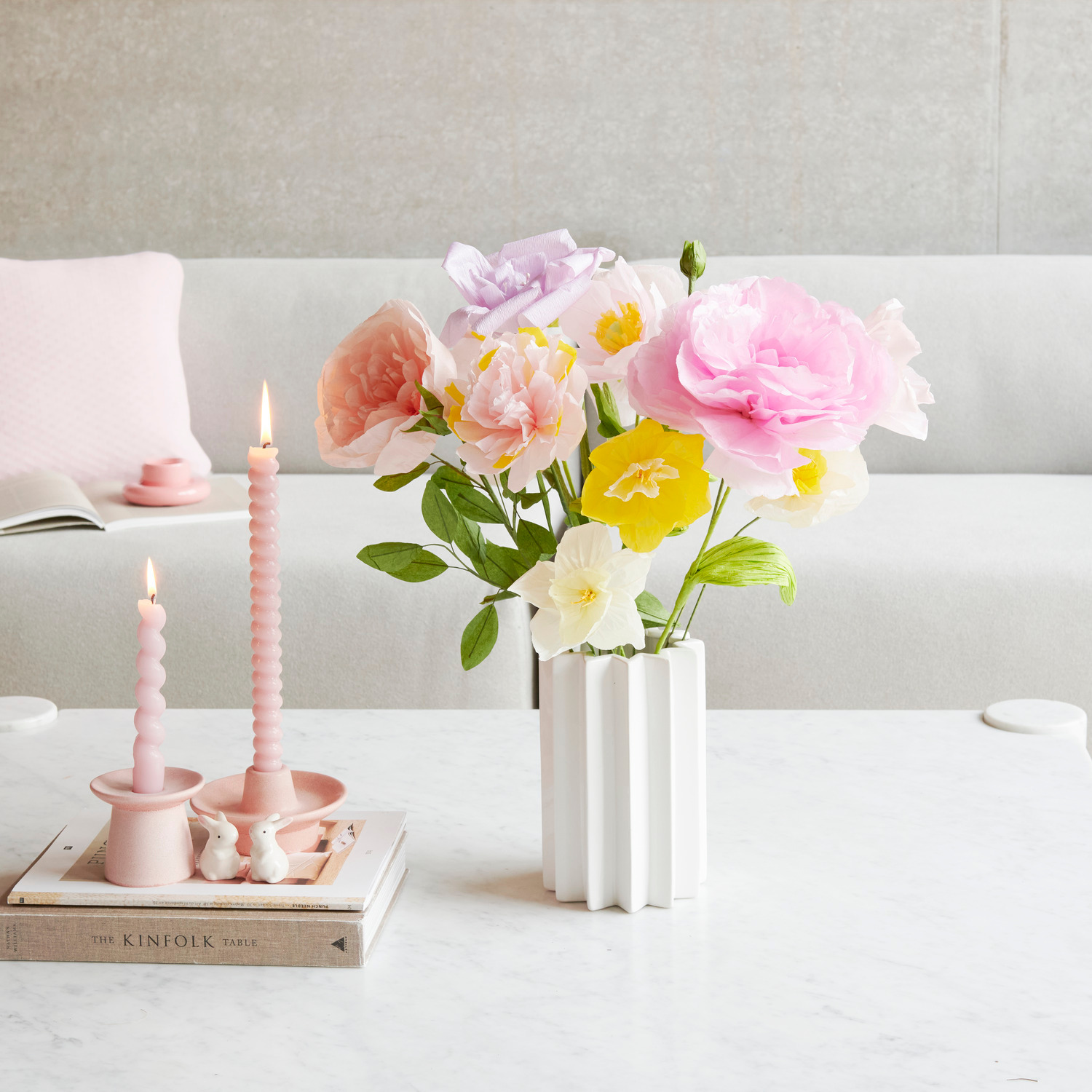 Kerzenhalter Porzellan Rosa mit Spiralkerzen und Keramik Hase auf Tisch. Weiße Vase mit bunten Papierblumen im Hintergrund.