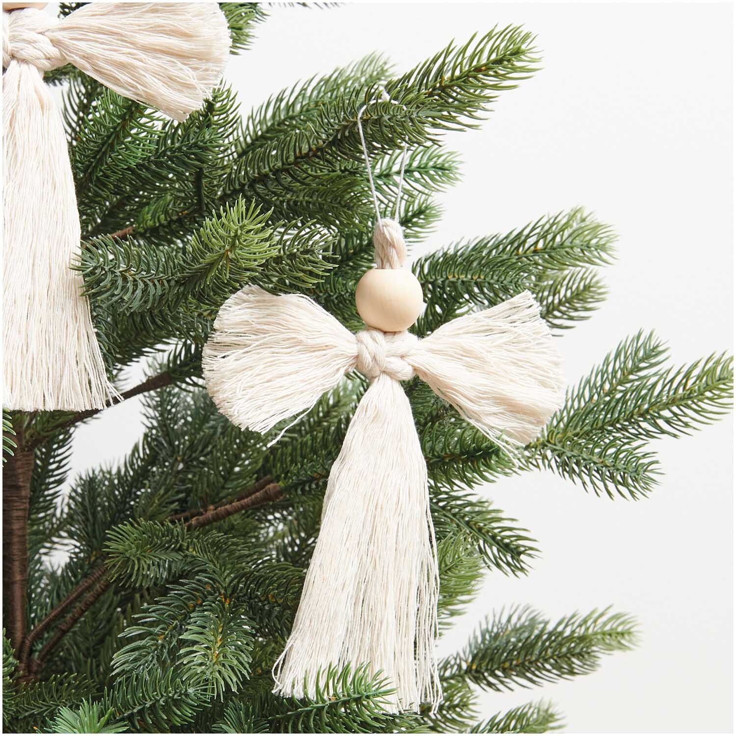 Set macramé ange 3 pièces 15x13xm from Rico Design Makramee Set Engel 3 Stück 15x13cm: Handgefertigter Engel aus beigem Garn, hängend an einem grünen Tannenbaum.