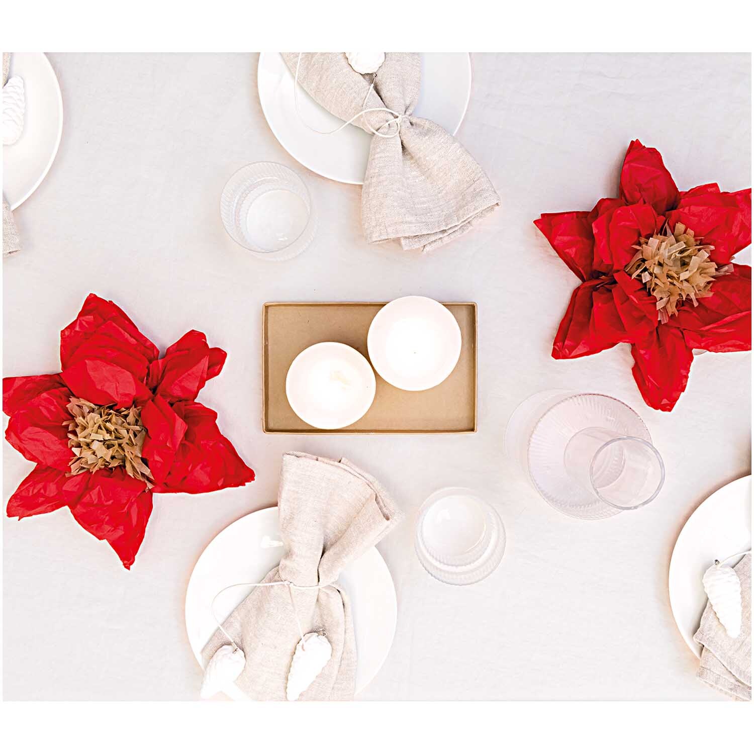 Seidenpapierblumen Weihnachtsstern 25cm 2 Stück dekorieren einen Tisch mit weißen Tellern und Kerzen, ideal für festliche Anlässe.