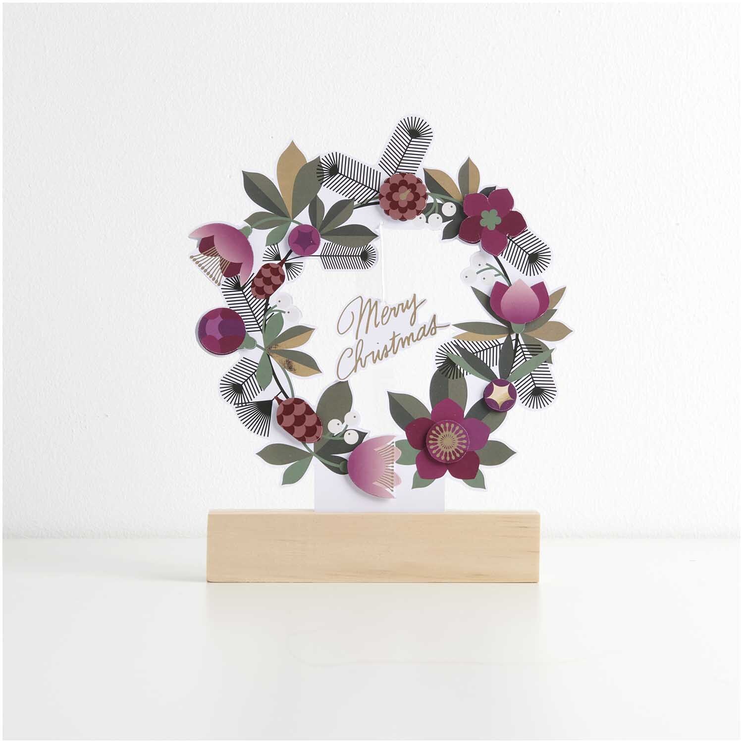 Paper Poetry bloc de papier à motif Christmas Rocks ! 24 feuilles from Rico Design Paper Poetry Motivpapierblock Christmas Rocks! zeigt einen dekorativen Weihnachtskranz mit bunten Blumen und Blättern auf einem Holzständer.