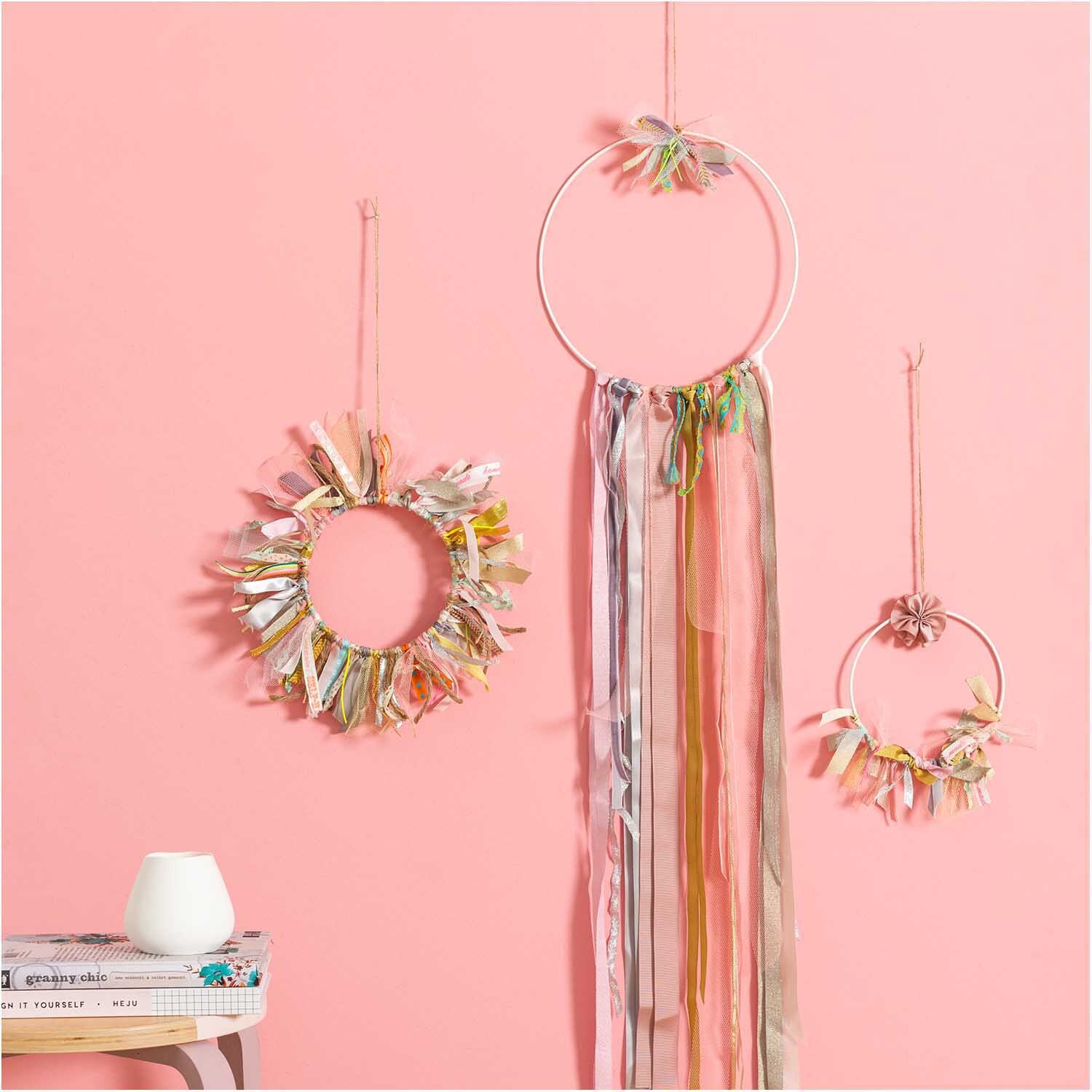 Metallring weiß matt von Rico Design, dekoriert mit bunten Bändern und Federn vor rosa Wand.