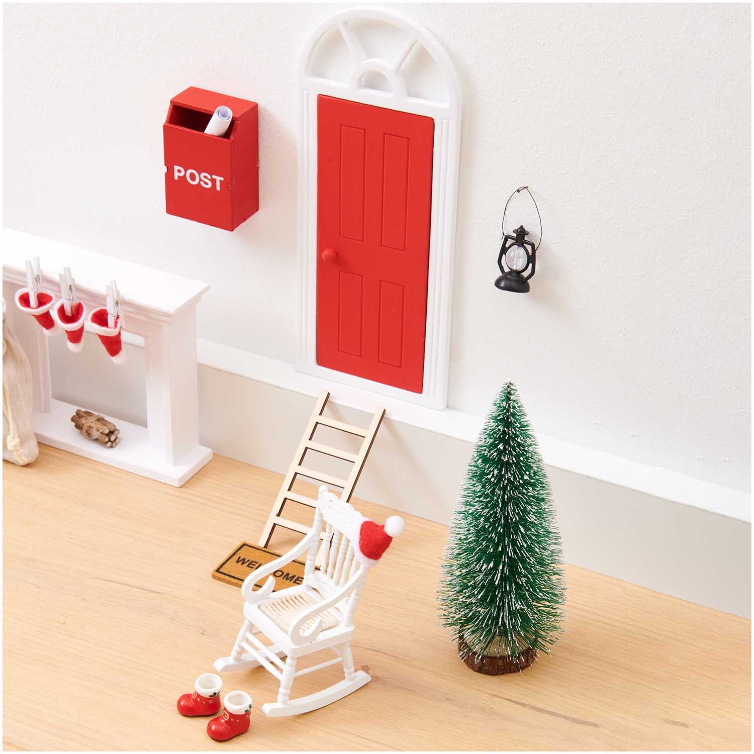 Miniatur Wichteltür mit Bogen, umgeben von Weihnachtsdeko: Schaukelstuhl, Leiter, Baum und Postkasten.