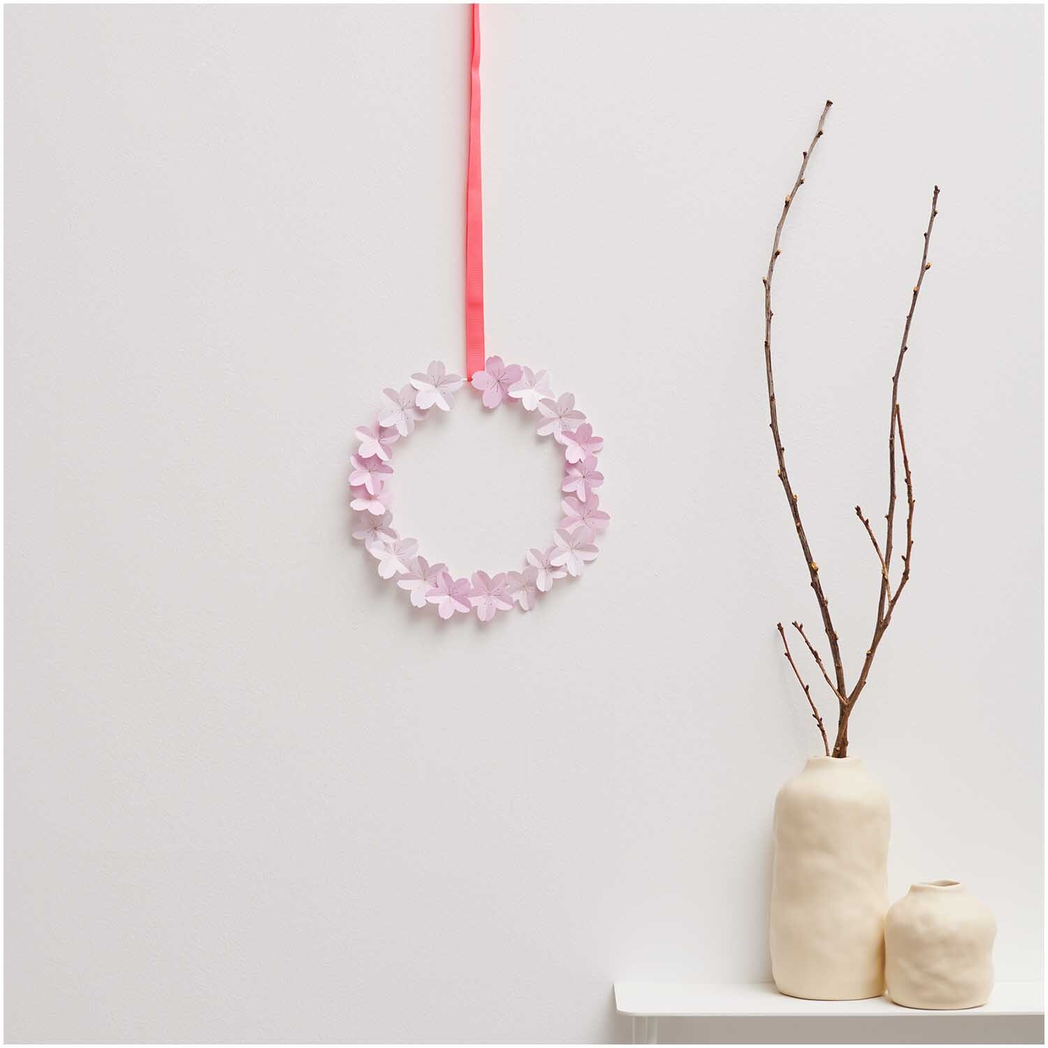 Paper Poetry Mini-Papierblüten Luxury Sakura, dekorativer Kranz aus rosa Papierblüten an rotem Band, neben minimalistischen Vasen.