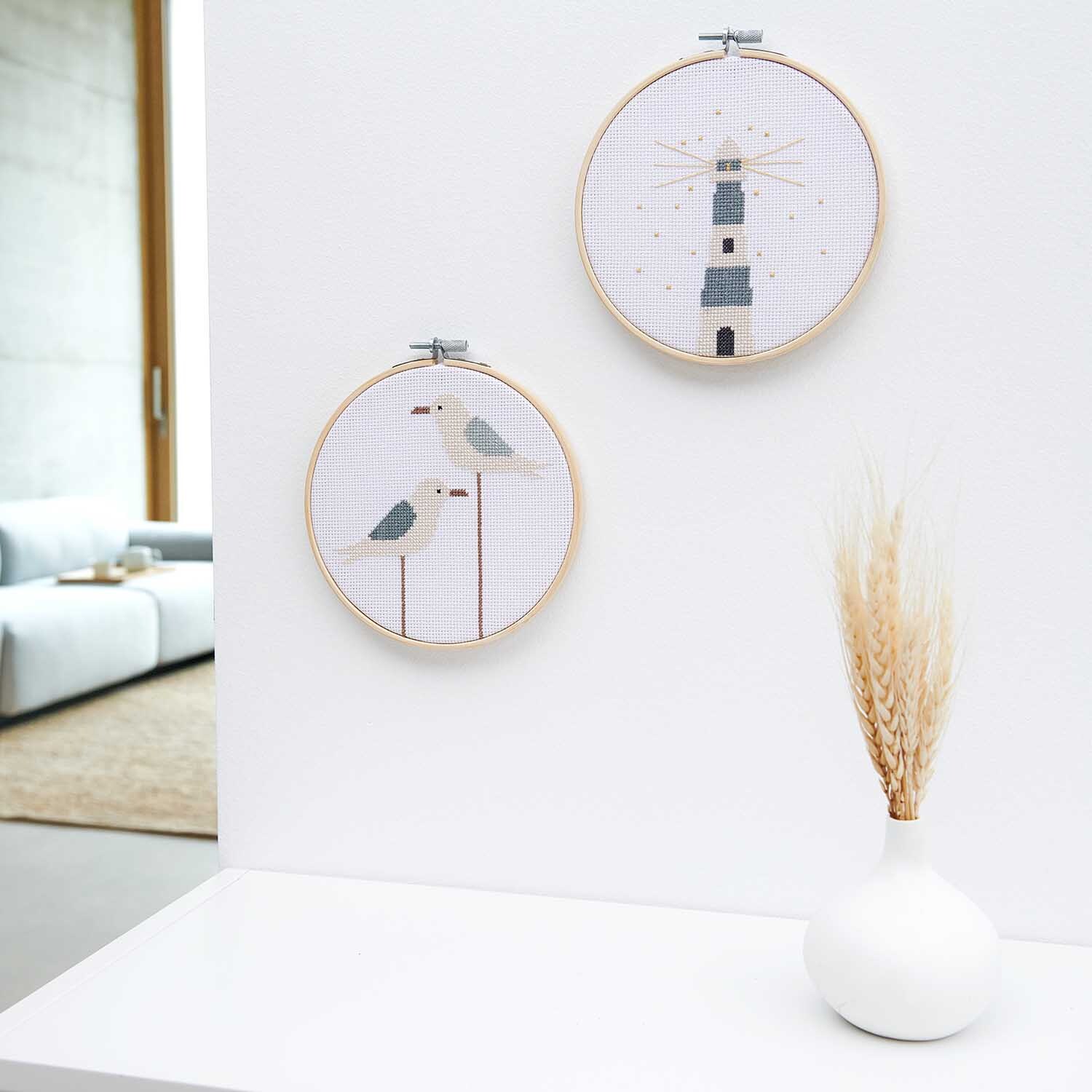 Paquet à broder Image phare Ø 15cm from Rico Design Stickpackung Leuchtturm Bild Ø 15cm von Rico Design zeigt zwei Stickrahmen mit Leuchtturm- und Möwenmotiv an einer weißen Wand.