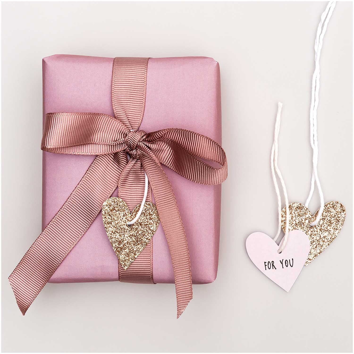 Paper Poetry Papieranhänger Herzen Glitter roségold 3x3,5cm 24 Stück von Rico Design Paper Poetry Papieranhänger in Herzform mit Glitter in Roségold neben rosa Geschenk mit Schleife.