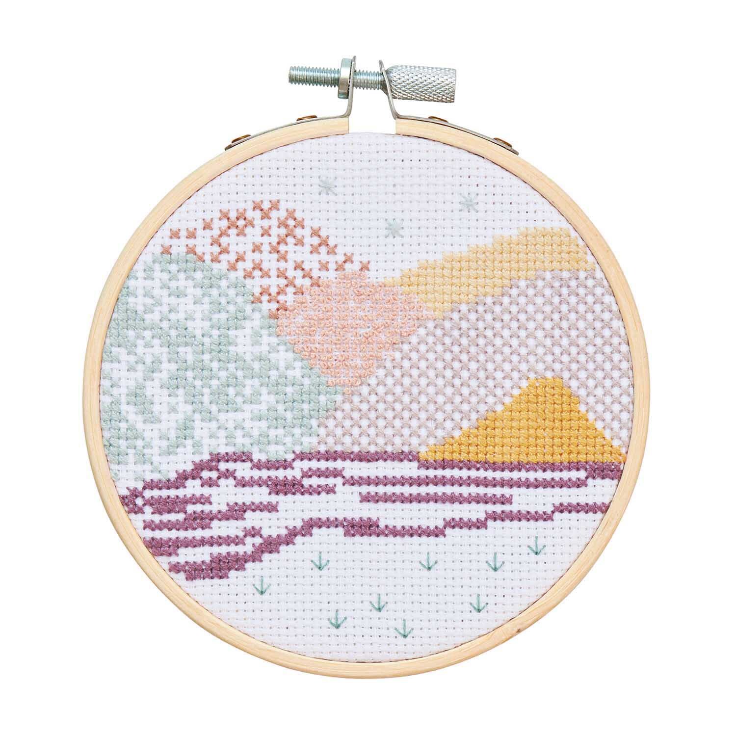 Stickpackung Mini Kit Landschaft Bild Ø 10cm zeigt eine bunte Landschaft in Pastelltönen im Stickrahmen. Ideal für kreative Handarbeitsprojekte.