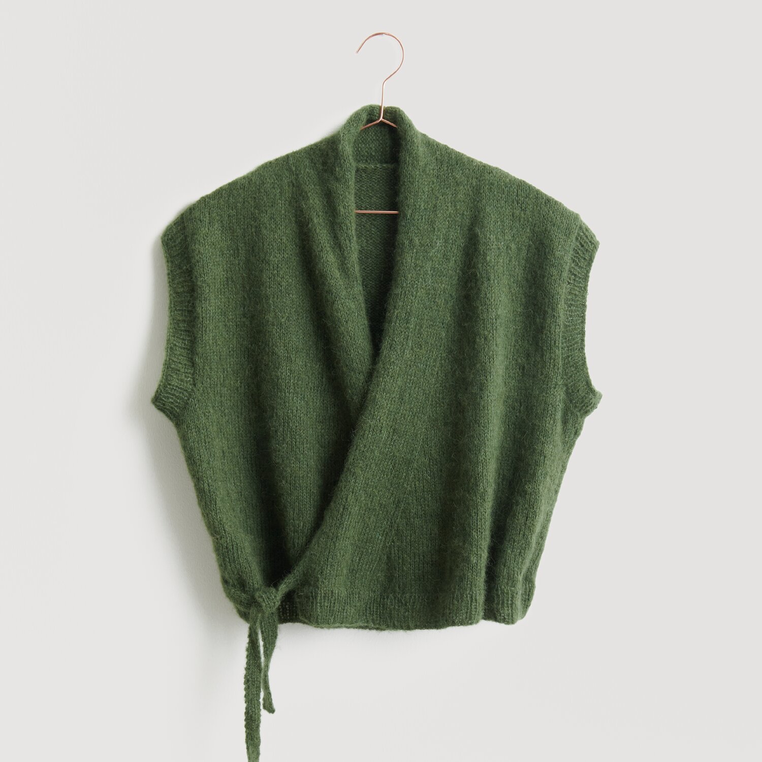 Luxury Alpaca Cotton Fusion 50g 190m Farbe Aloe von Rico Design Grüne Strickweste von Modell Legeware, präsentiert auf einem Kleiderbügel. Die Weste hat kurze Ärmel und einen Wickelstil mit Bindeband, ideal für einen lässigen Look.