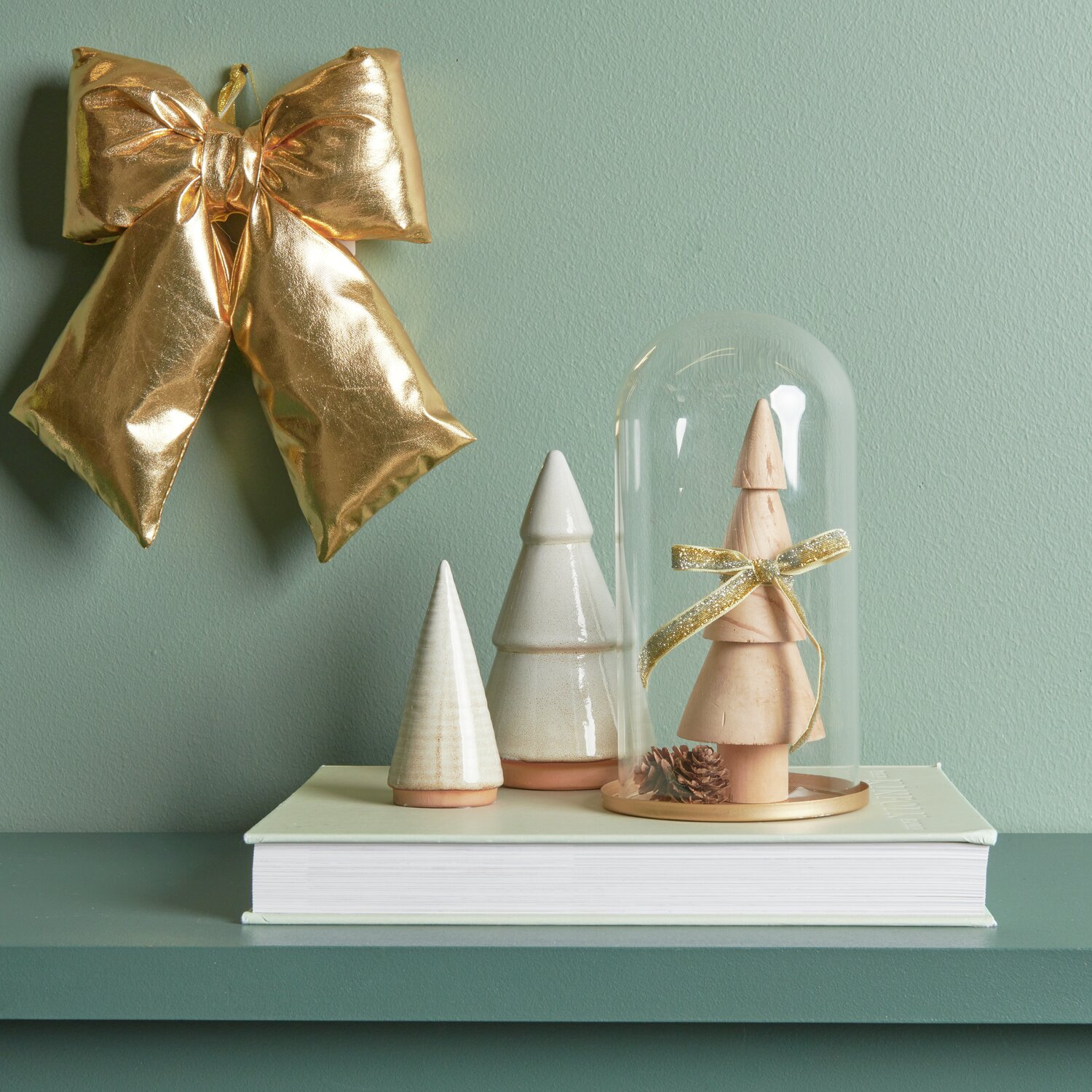 Porzellan Tannenbaum Altweiß und Beige, dekoriert mit goldener Weihnachtsschleife und Glashaube auf einem Buch.