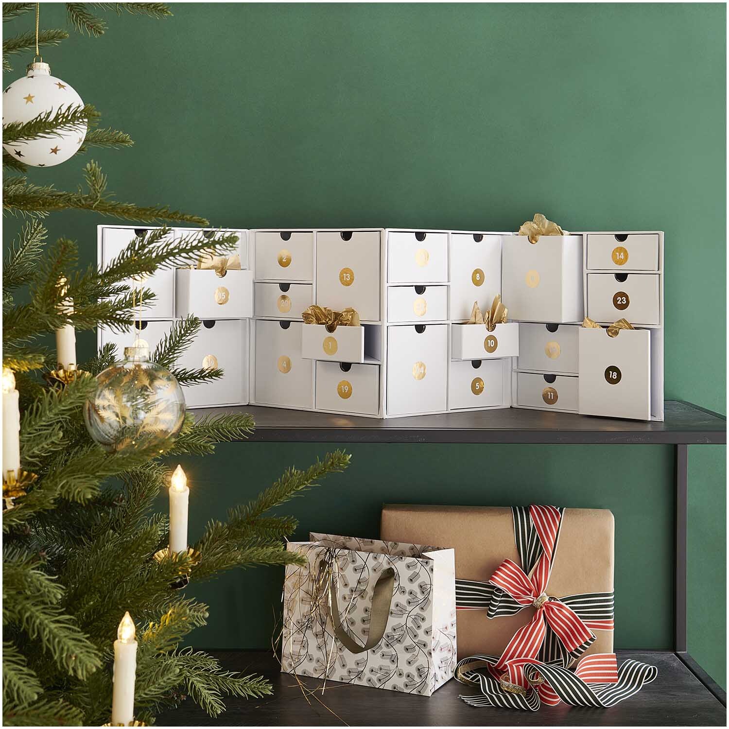 Schubladenschränkchen zum Aufklappen weiß gold 24x32x16cm von Rico Design Schubladenschränkchen zum Aufklappen auf Regal, dekoriert mit goldenen Akzenten, neben Weihnachtsbaum. Ideal für festliche Aufbewahrung.
