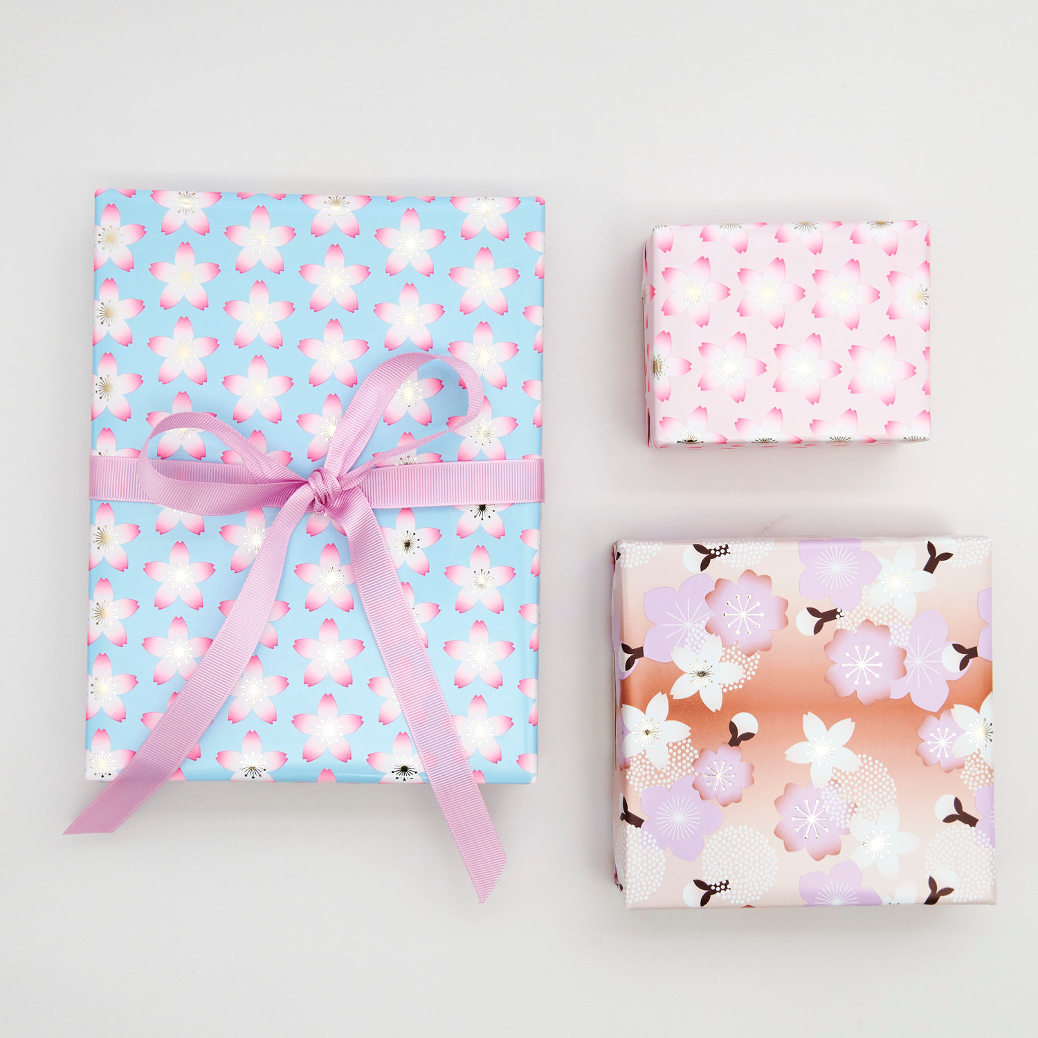 Geschenkpapier Kirschblüten Orange 70cm 2m 80g/m² von Rico Design Geschenkpapier Kirschblüten Pink: Drei Geschenke mit Kirschblütenmuster in Rosa, Blau und Orange, verpackt mit Rico Design Papier.