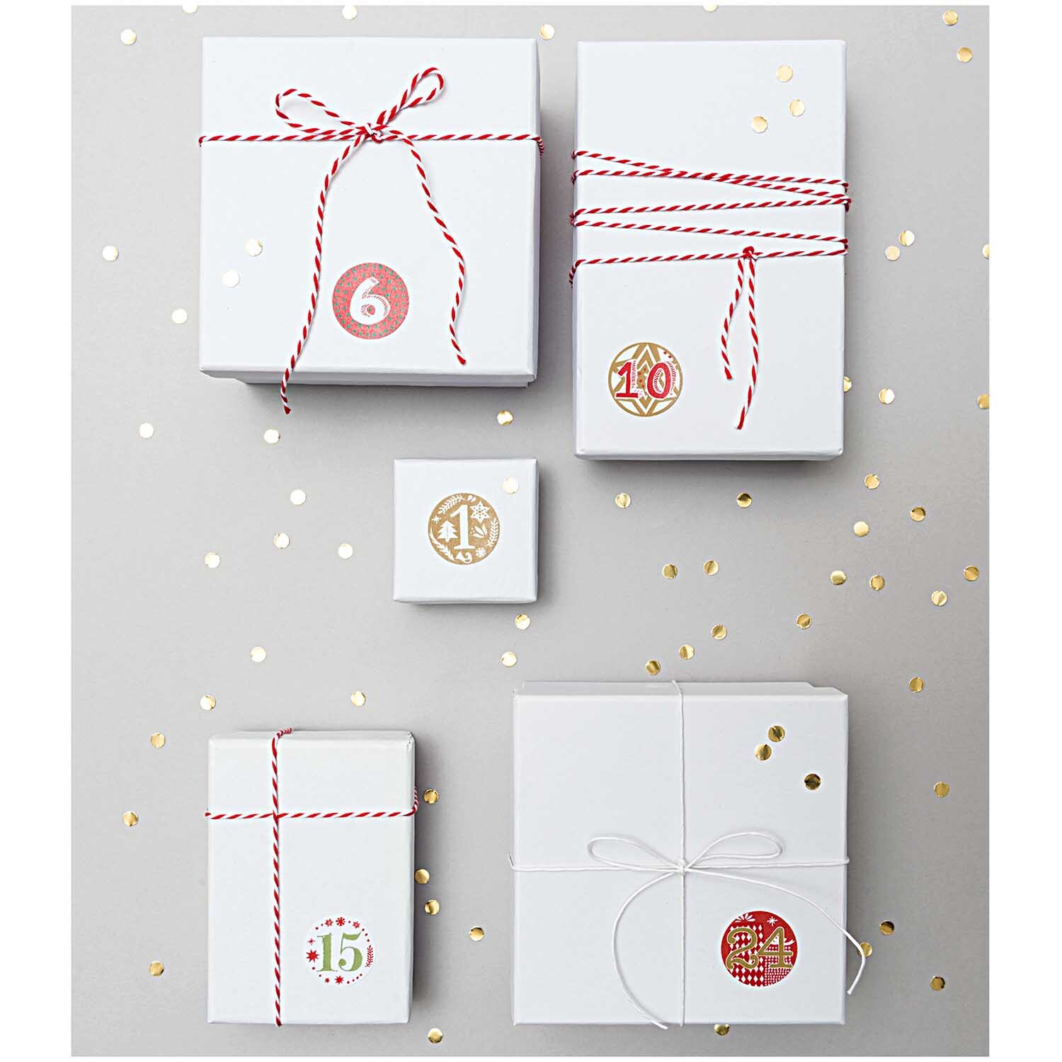 Paper Poetry Adventskalender Sticker auf Geschenken mit roten und grünen Zahlen, dekoriert mit Bändern. Ideal für kreative Weihnachtsdekoration.
