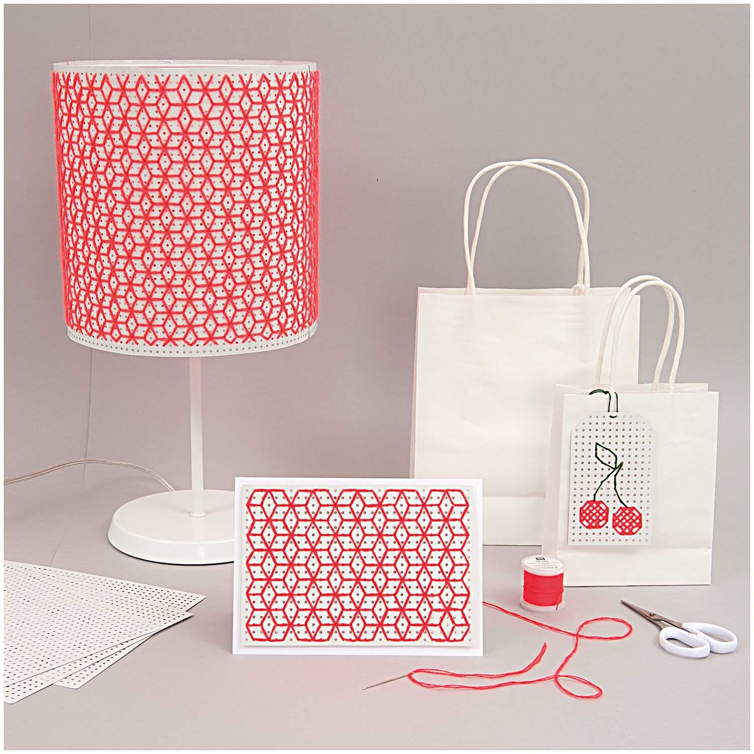 Präzisionsschere groß 16,5cm von Rico Design Präzisionsschere groß 16,5cm neben Bastelmaterialien: rote Fadenrolle, weiße Taschen und Lampe mit rotem Muster.