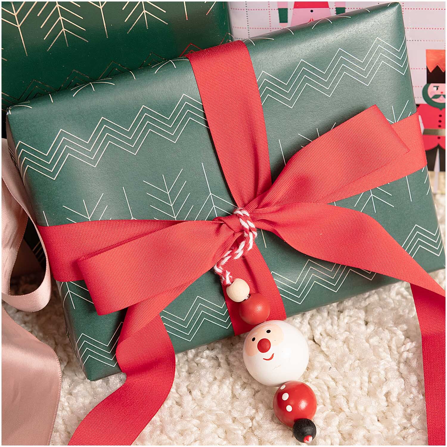 Holzhänger Santa aus Holzkugeln rot-weiß 3x16cm von Rico Design Holzhänger Santa aus Holzkugeln schmückt ein Geschenk mit rotem Band, ideal für festliche Dekorationen.