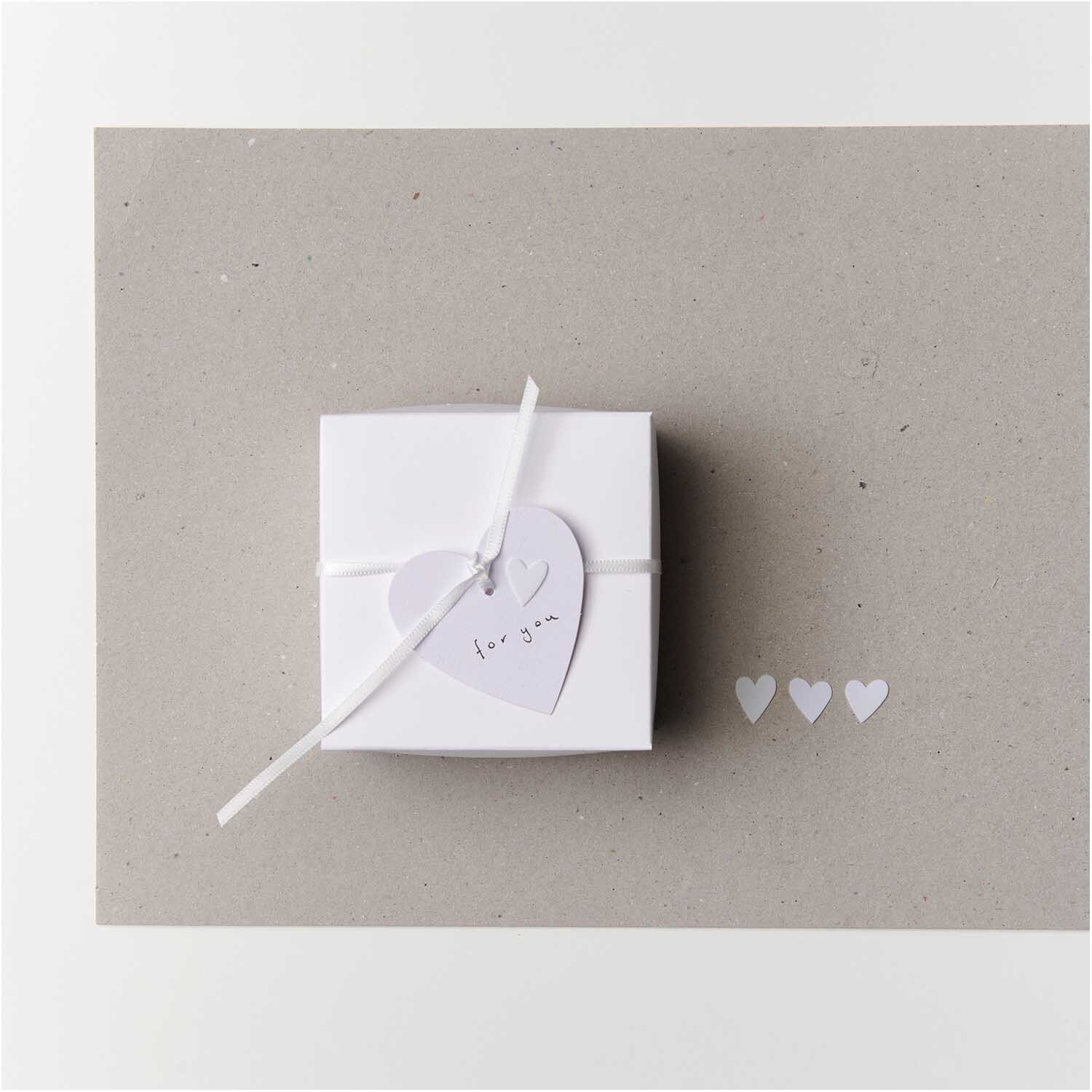 Flitter Herz 100 Stück Farbe Weiß von Rico Design Flitter Herz 100 Stück: Weiße Papierherzen von Rico Design neben einer Geschenkbox auf grauem Hintergrund.