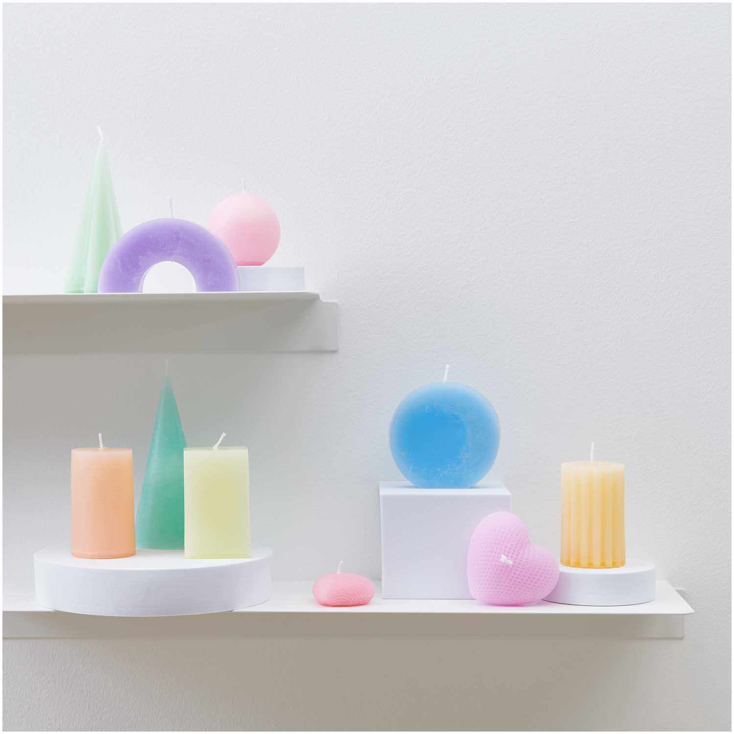 Kerzengießform Zylinder 61x61x90mm: Bunte Kerzen in Pastellfarben auf weißen Regalen arrangiert.