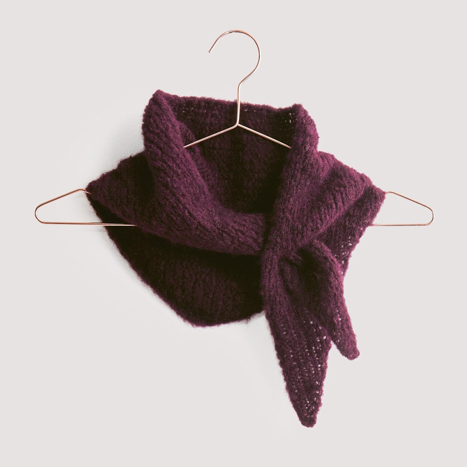 Strickset Dreieckstuch Modell 04 aus Luxury Knits, weinrot, auf Kupferbügel vor grauem Hintergrund.