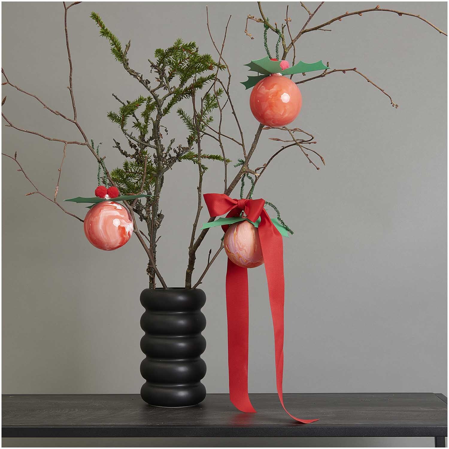 Weihnachtskugel aus Kunststoff 10cm von Rico Design Weihnachtskugel aus Kunststoff 10cm an einem Ast in schwarzer Vase, dekoriert mit rotem Band.