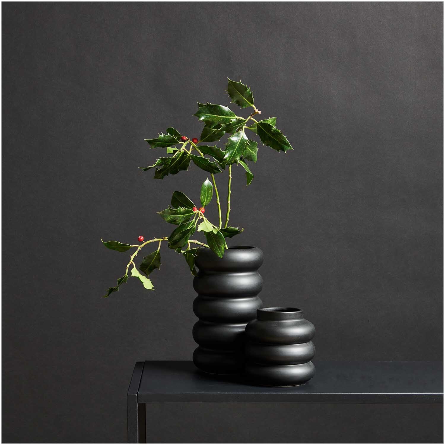 Keramik Vase schwarz von Rico Design auf einem Tisch, mit grünen Zweigen dekoriert. Elegantes, modernes Design.