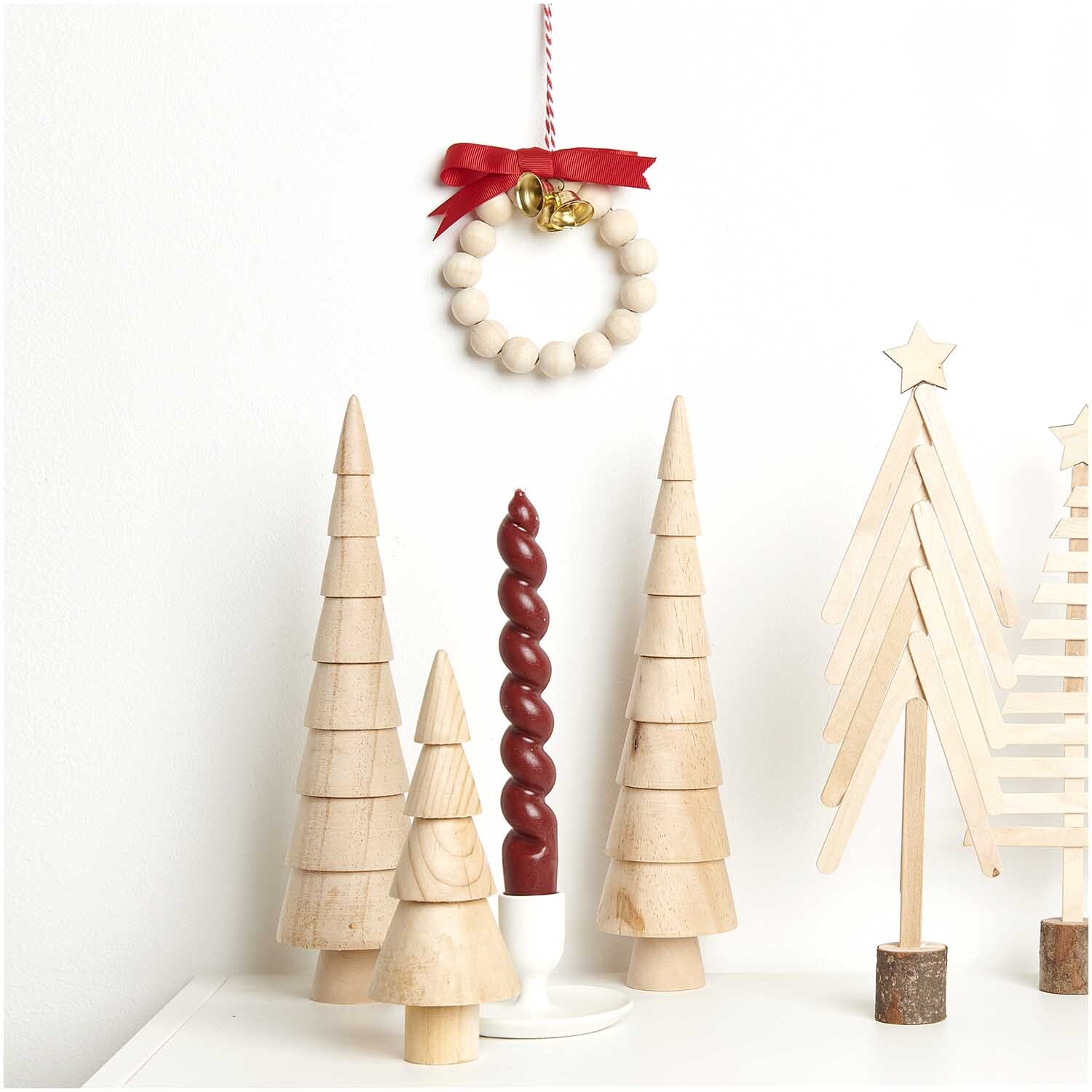 Bastelset Holzperlen Kranz natur 24-teilig von Rico Design Bastelset Holzperlen Kranz natur: Ein dekorativer Kranz aus Holzperlen mit rotem Band, umgeben von Holz-Weihnachtsbäumen. Ideal für kreative Dekorationen.